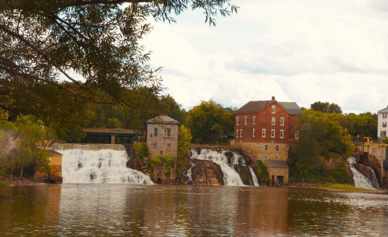 a waterfall is surrounded by buildings and trees called the Falls at Vergennes