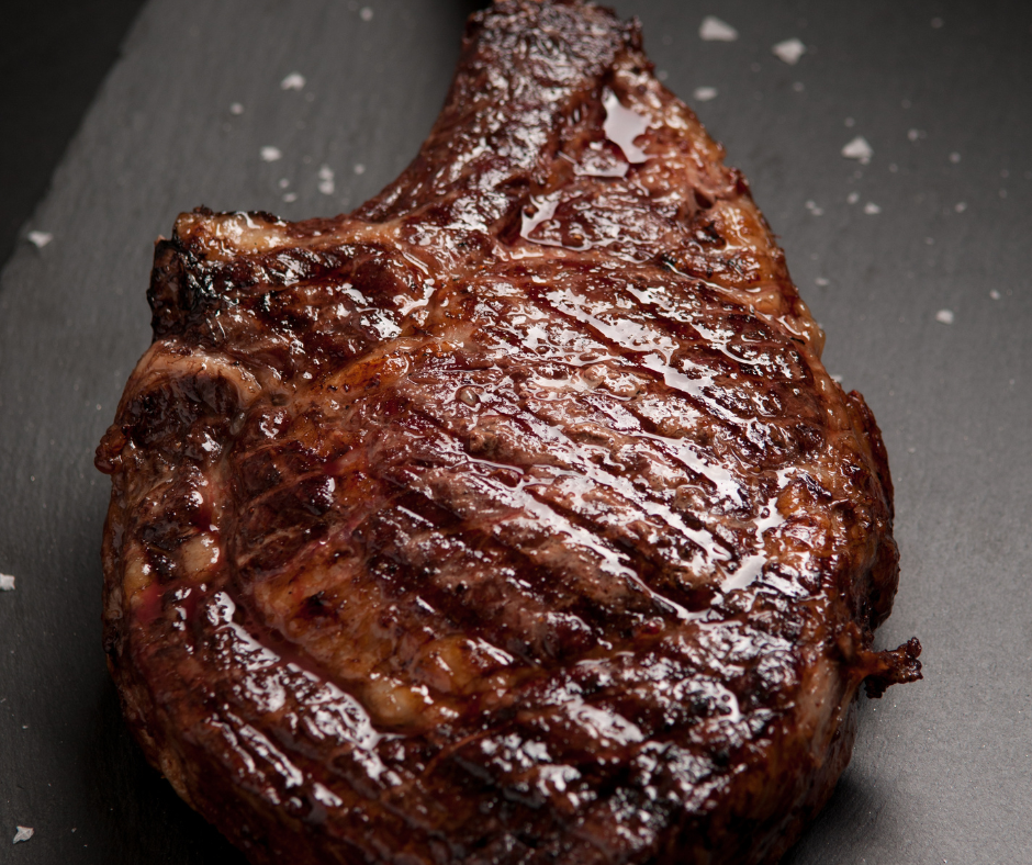 A close up of a steak on a black plate on a table.