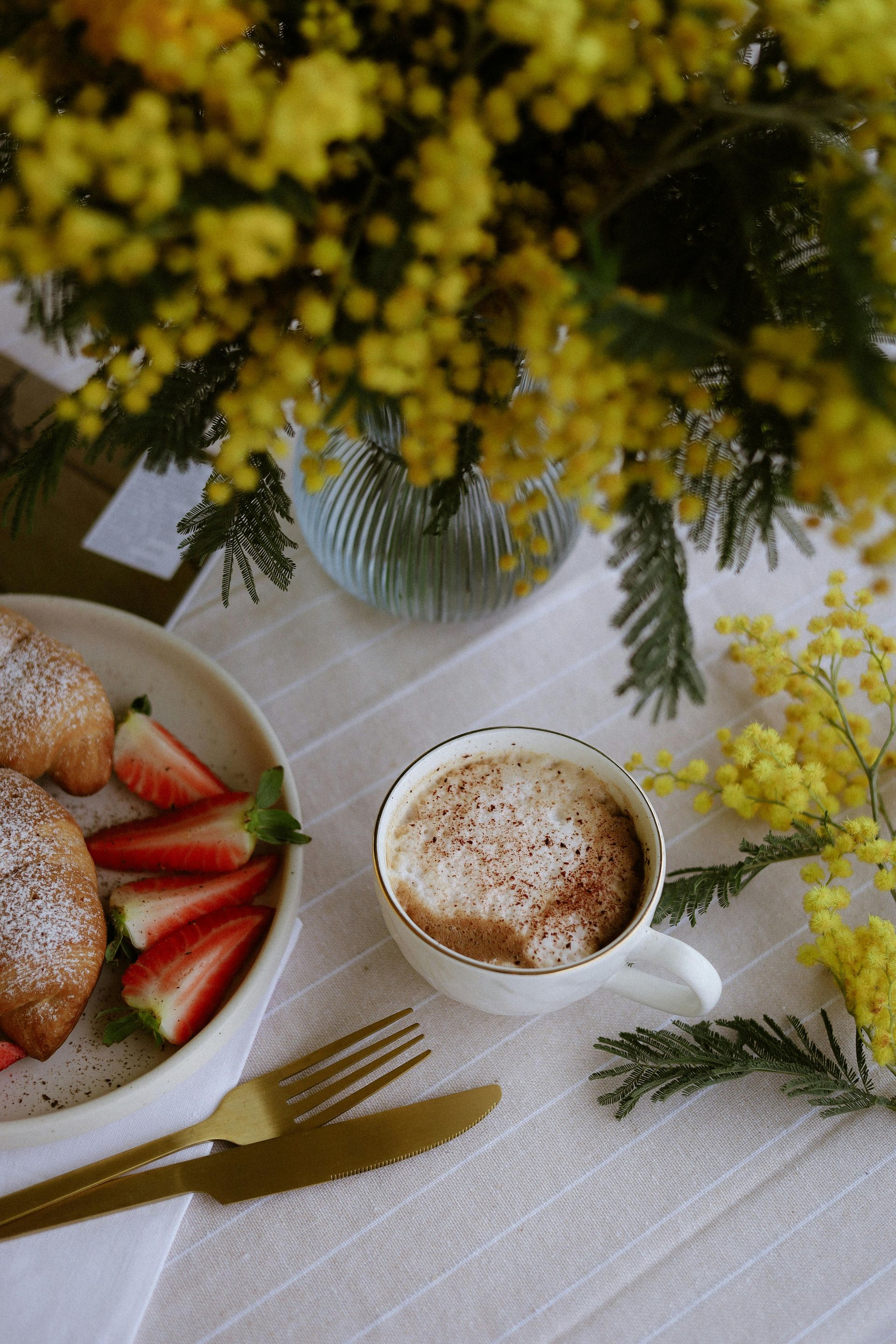 There is a bowl of strawberries and a cup of coffee on the table.