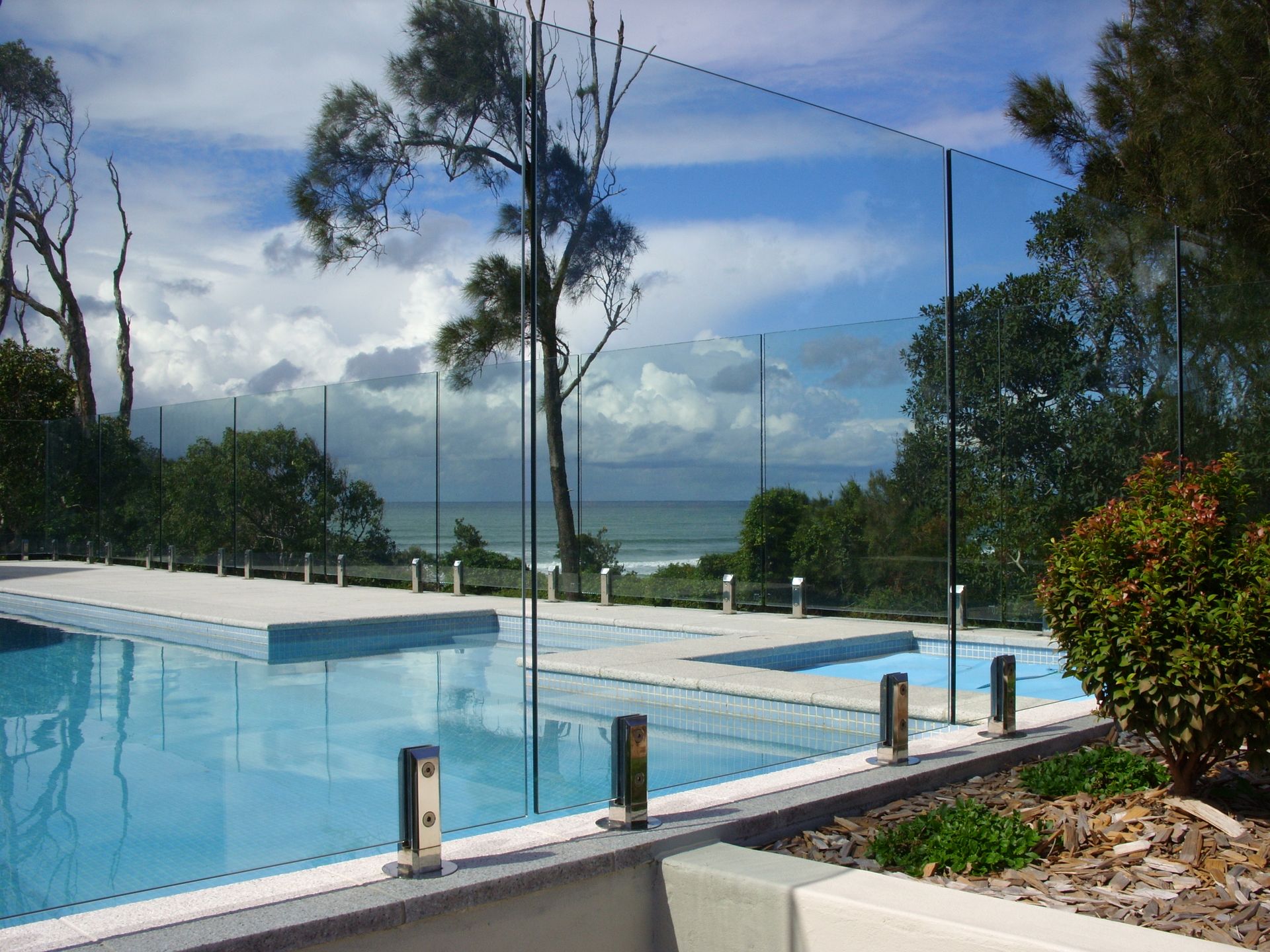 Swimming Pool Surrounded By Chairs With Glass Pool Fence — Fabricator In Coffs Harbour, NSW