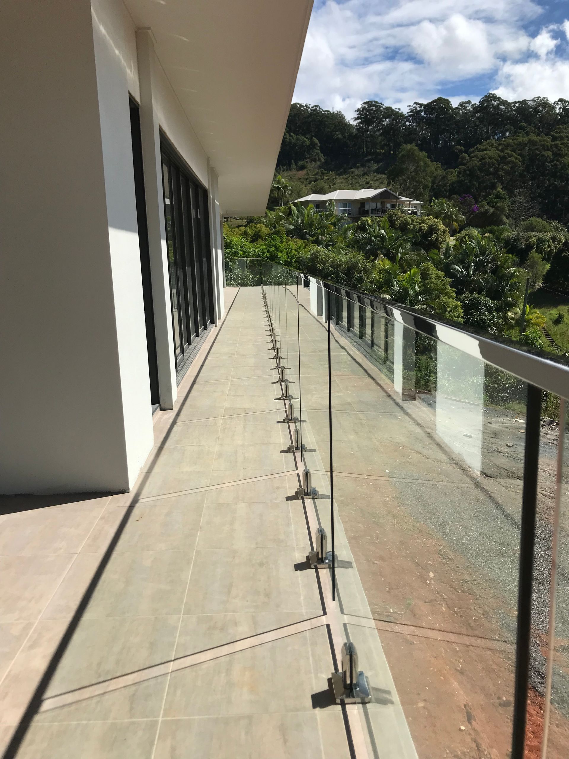 A balcony with a glass railing and trees in the background — Fabricator In Coffs Harbour, NSW