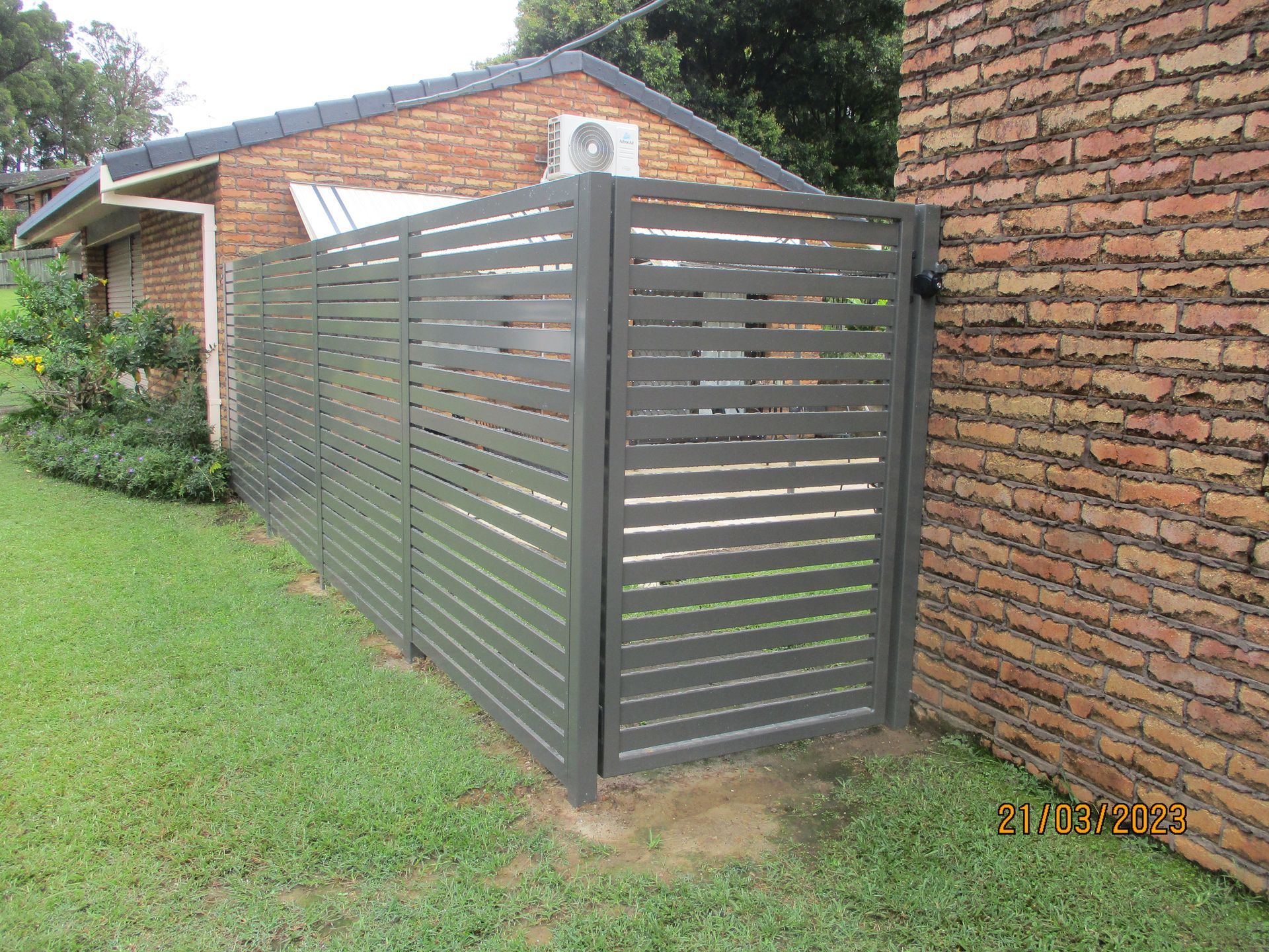 A fence is sitting next to a brick wall in front of a house — Fabricator In Coffs Harbour, NSW