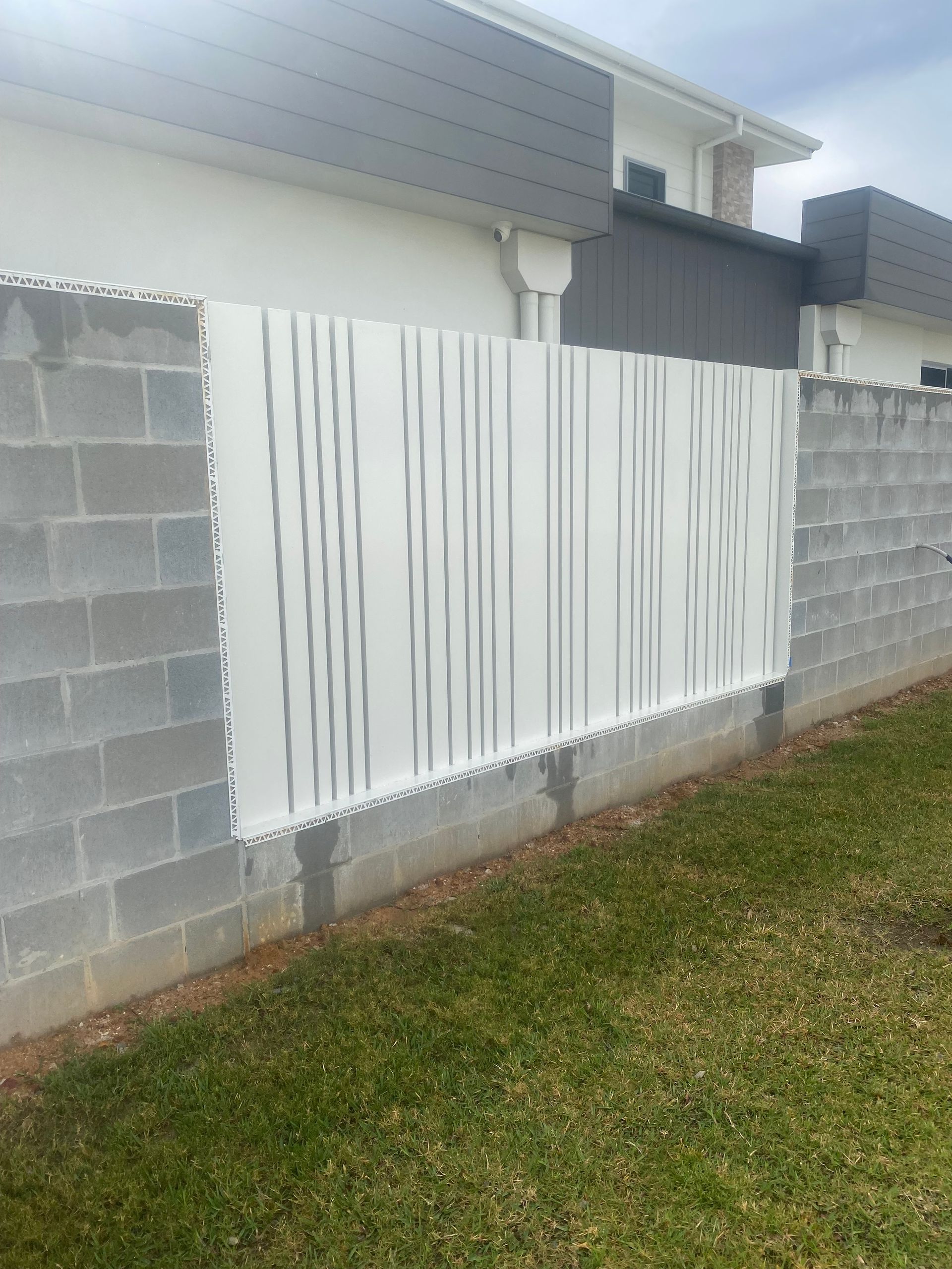 A white fence is sitting on top of a brick wall next to a house — Fabricator In Coffs Harbour, NSW
