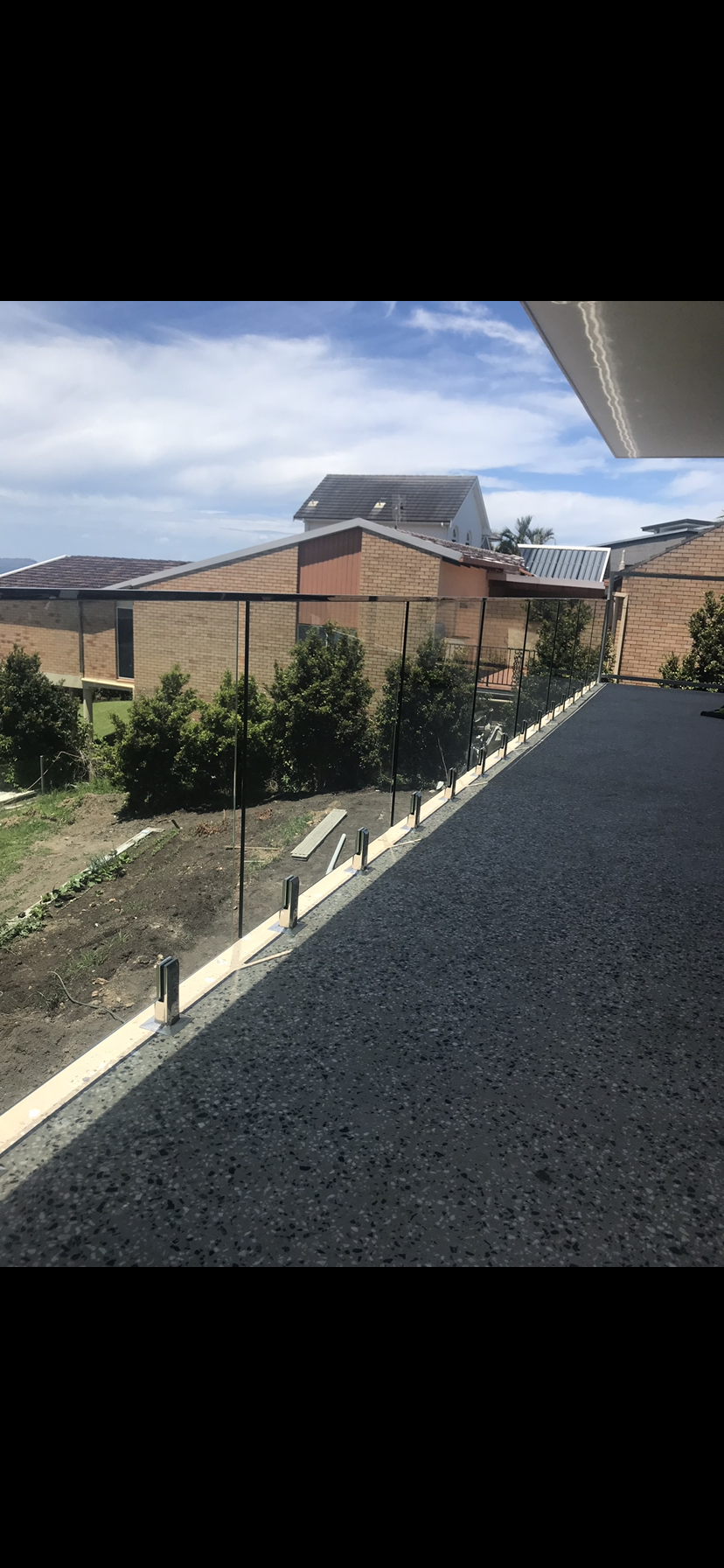 A balcony with a glass railing and a view of a house — Fabricator In Coffs Harbour, NSW
