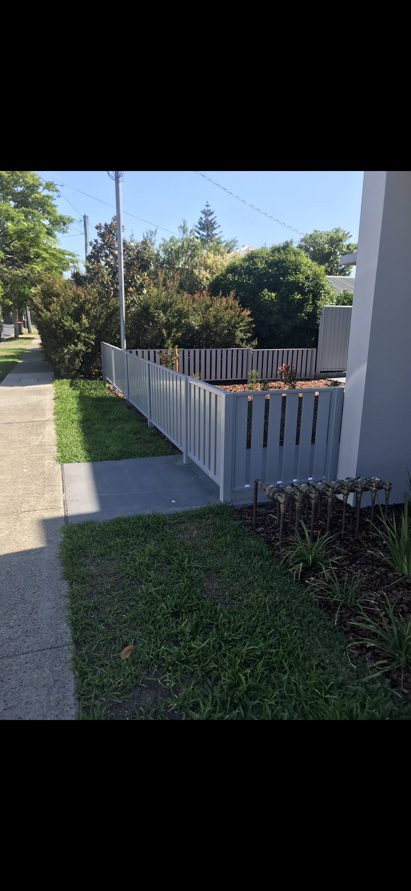 A white picket fence is sitting next to a sidewalk in front of a house — Fabricator In Coffs Harbour, NSW