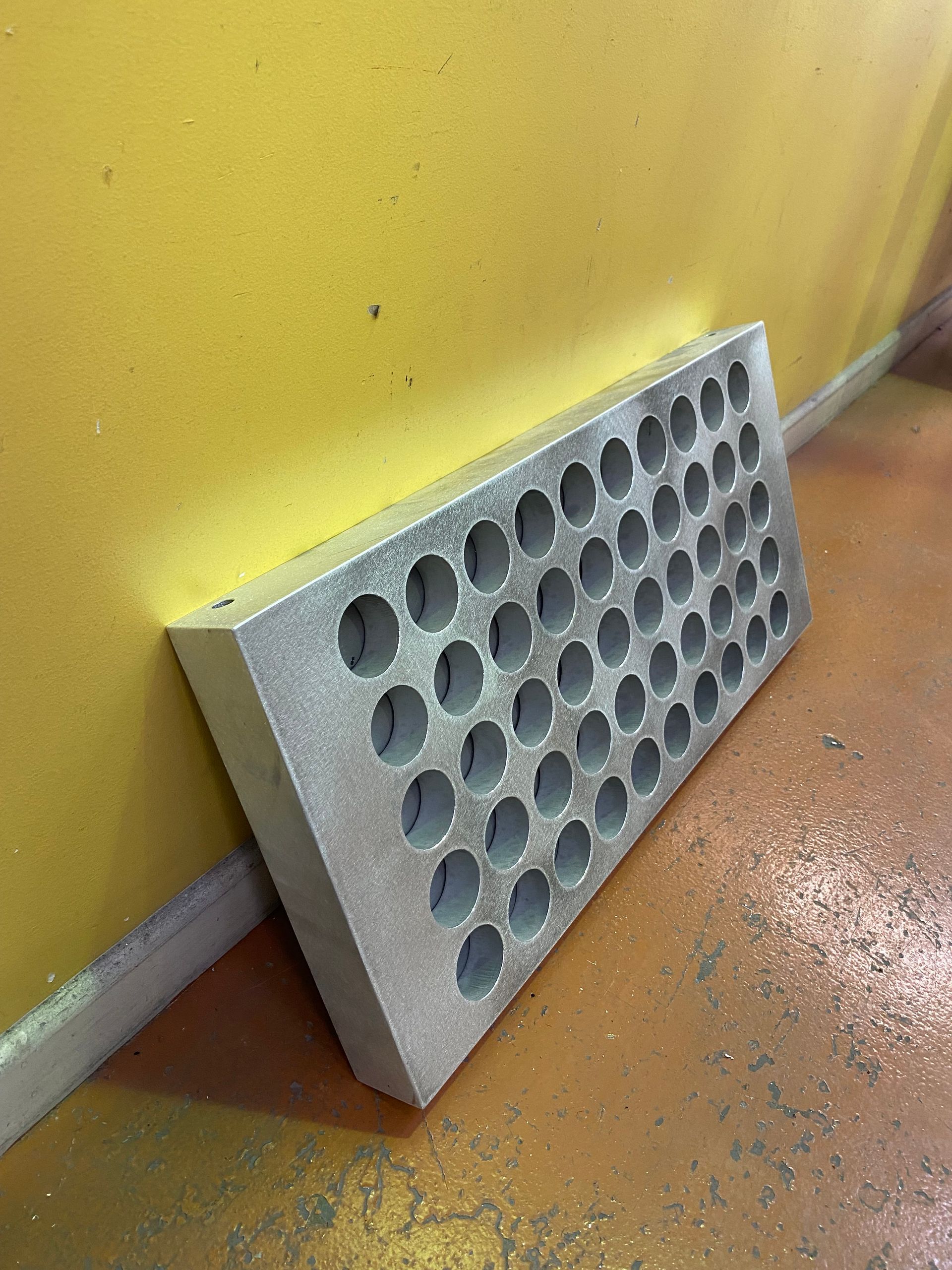 A metal block with holes in it is leaning against a yellow wall — Fabricator In Coffs Harbour, NSW