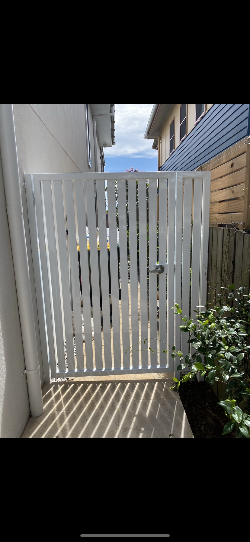 A white gate is between two buildings in a narrow alleyway — Fabricator In Coffs Harbour, NSW