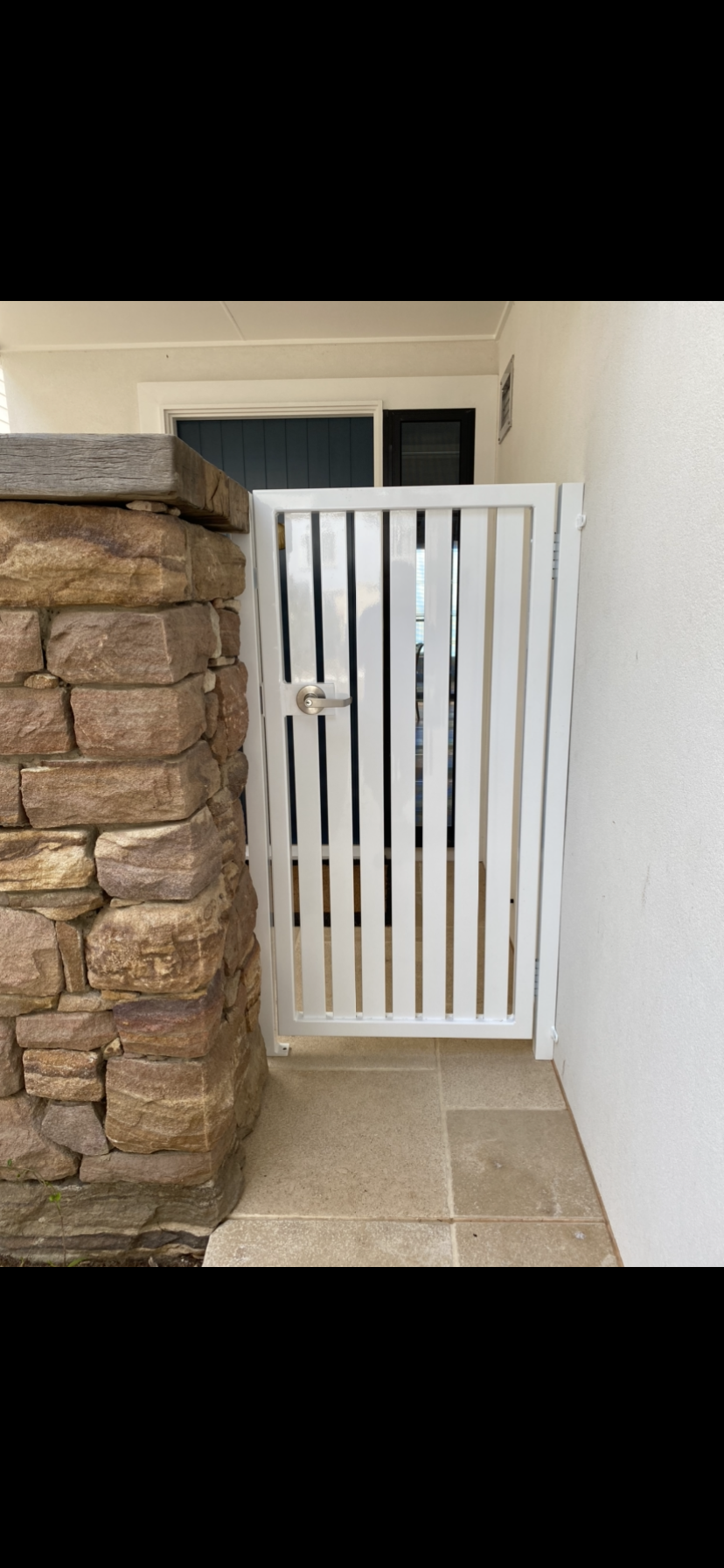 A white gate is sitting next to a stone wall — Fabricator In Coffs Harbour, NSW