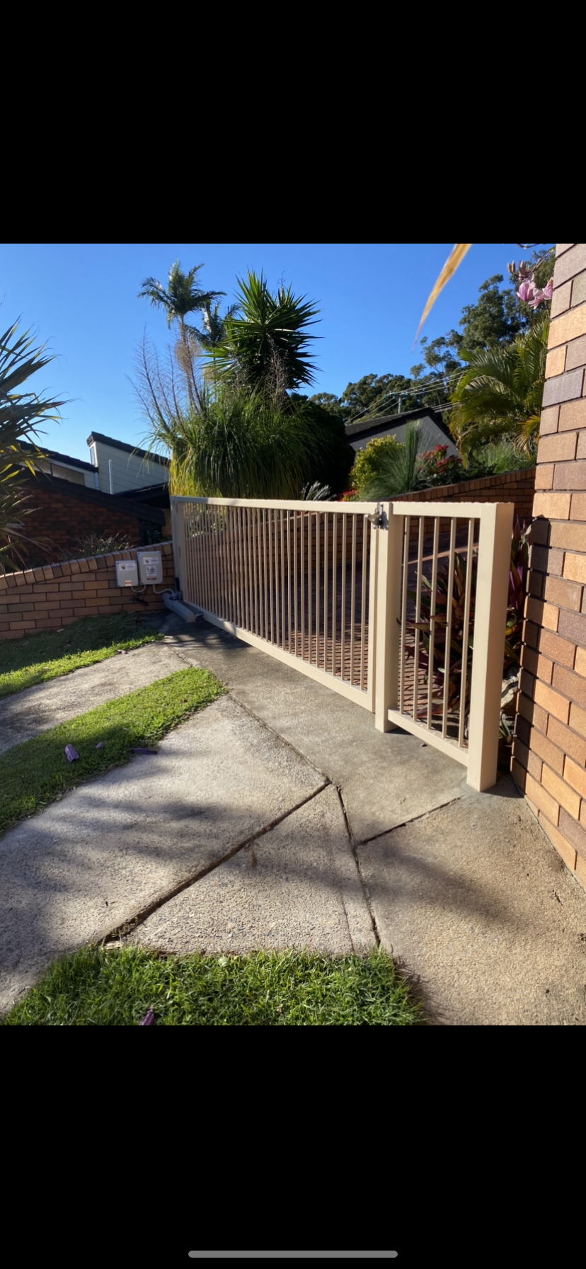 A fence is sitting on the side of a sidewalk next to a brick building — Fabricator In Coffs Harbour, NSW