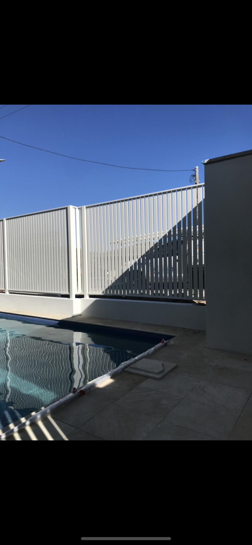 A white fence surrounds a swimming pool with a blue sky in the background — Fabricator In Coffs Harbour, NSW