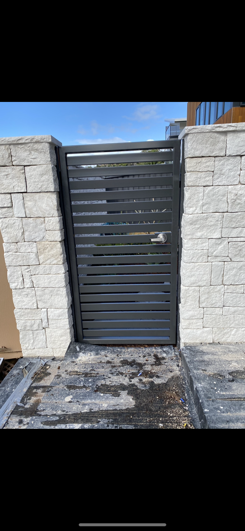 A black gate is sitting in front of a brick wall — Fabricator In Coffs Harbour, NSW