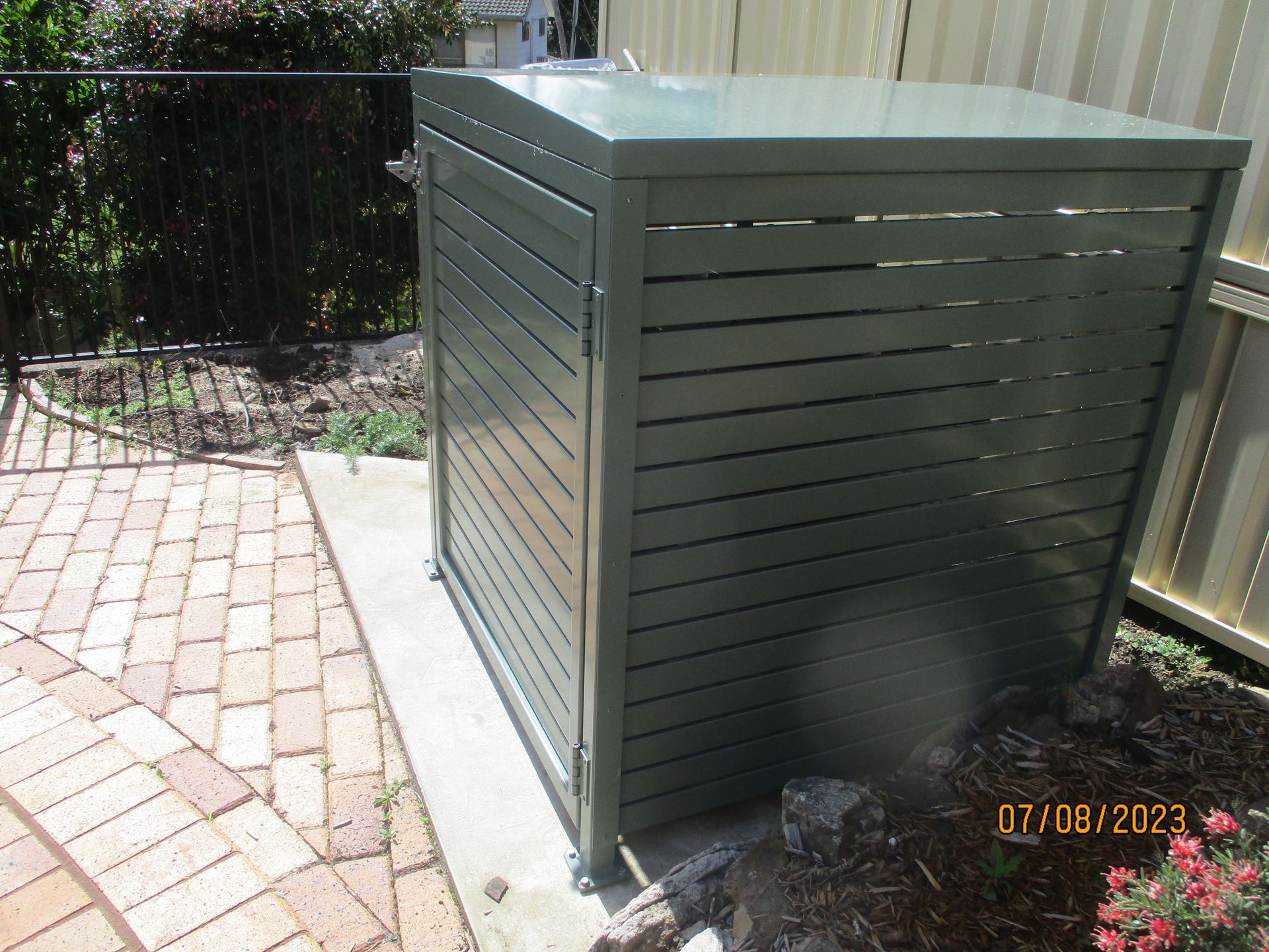 A green shed is sitting on a brick sidewalk next to a fence — Fabricator In Coffs Harbour, NSW