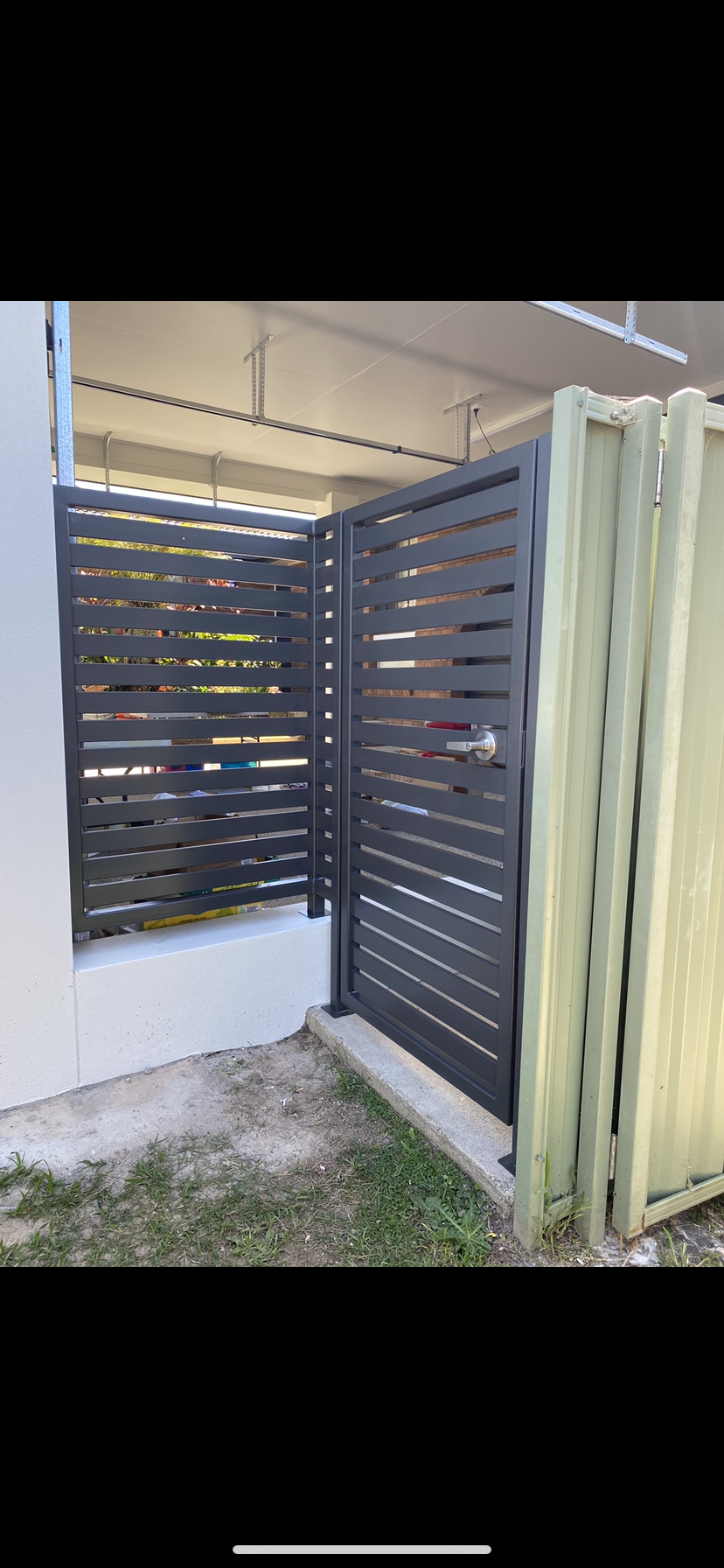 A black gate is sitting next to a white wall — Fabricator In Coffs Harbour, NSW