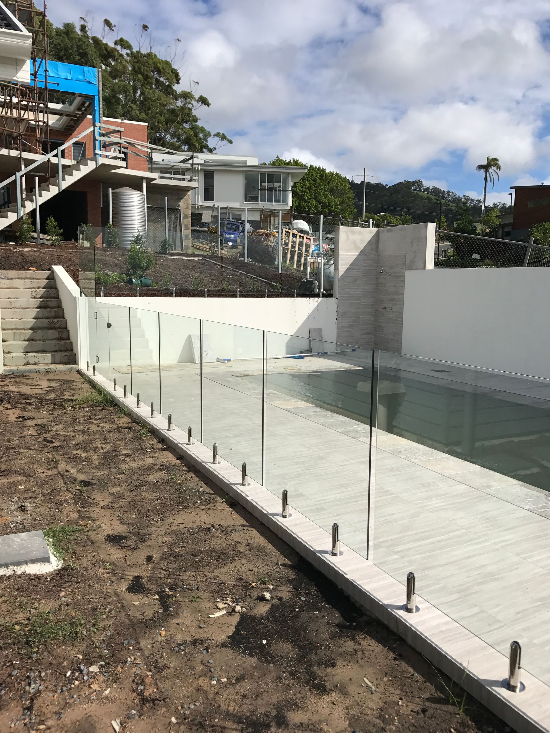 A swimming pool with a glass fence around it and a house in the background — Fabricator In Coffs Harbour, NSW