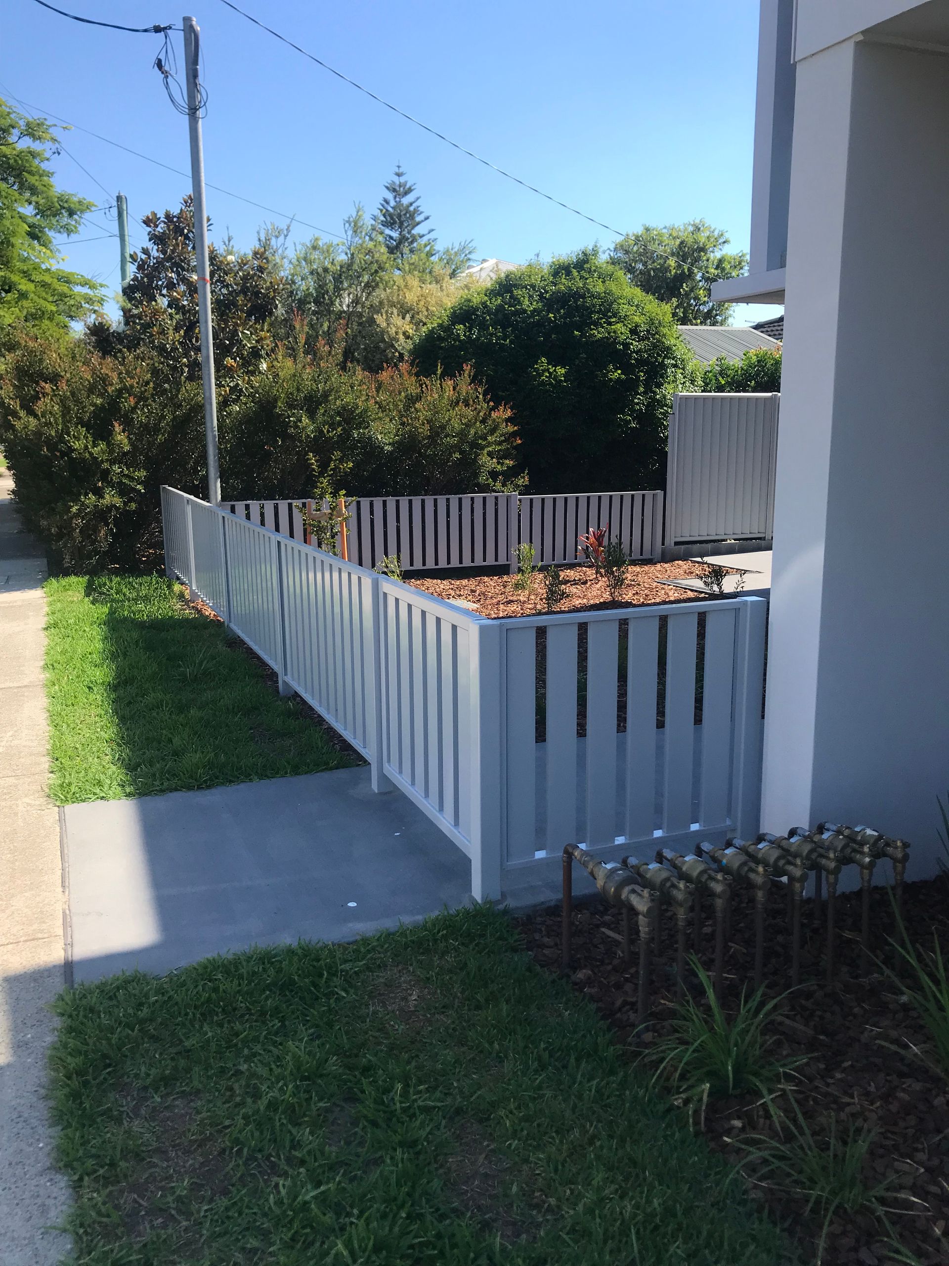 A white fence surrounds a grassy yard in front of a house — Fabricator In Coffs Harbour, NSW