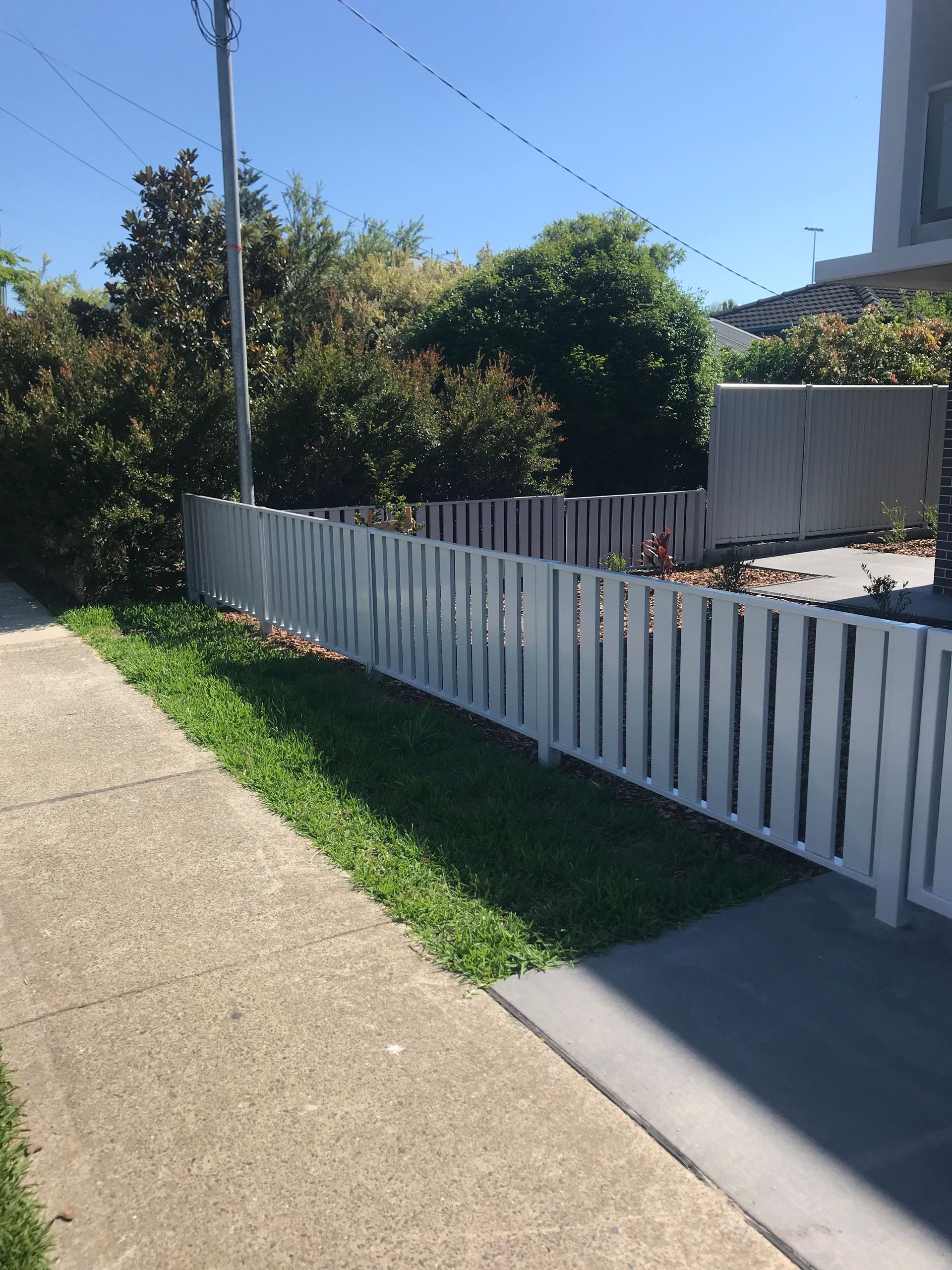 A white picket fence along a sidewalk in front of a house — Fabricator In Coffs Harbour, NSW