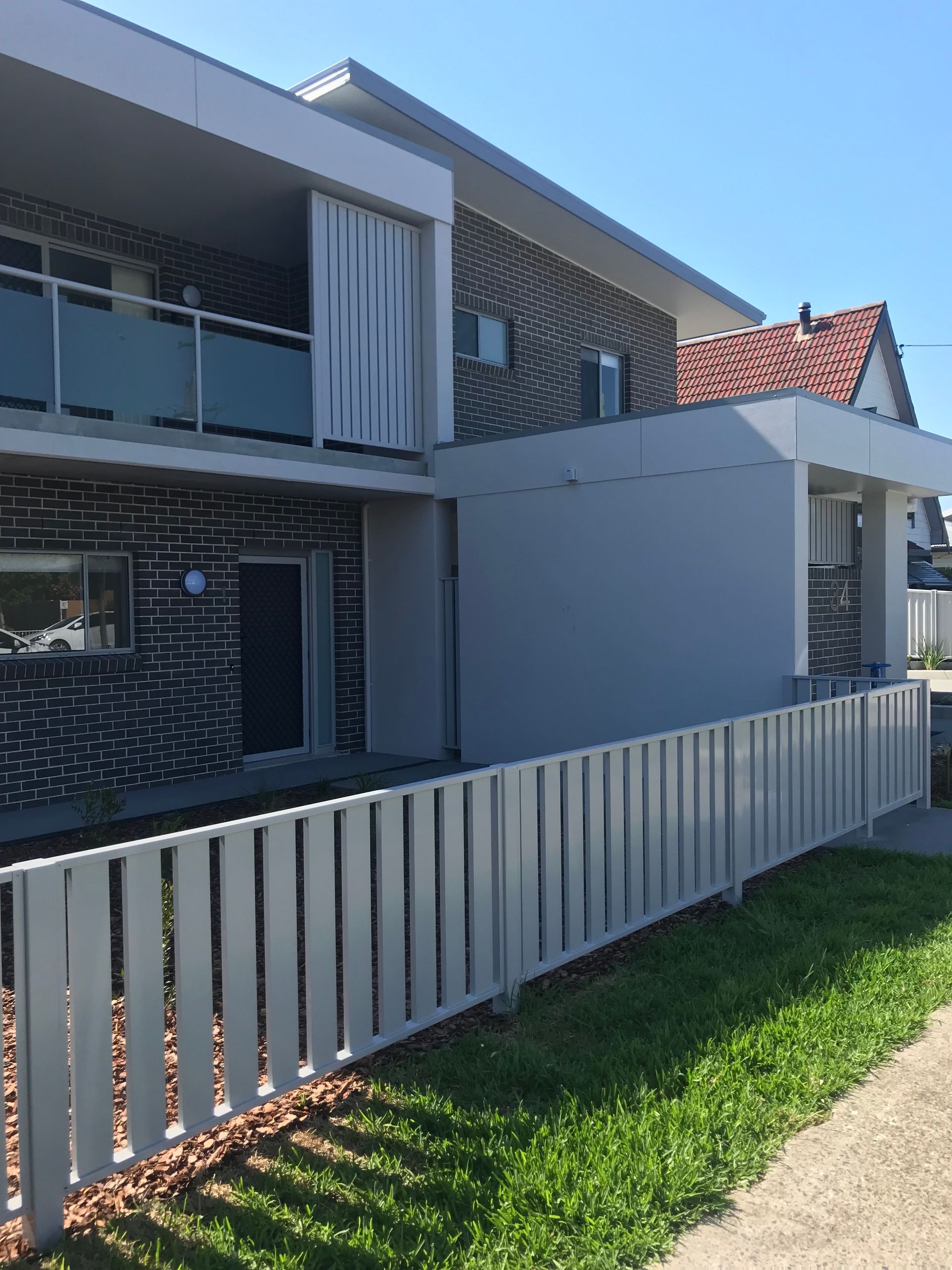 A white fence is in front of a brick building — Fabricator In Coffs Harbour, NSW