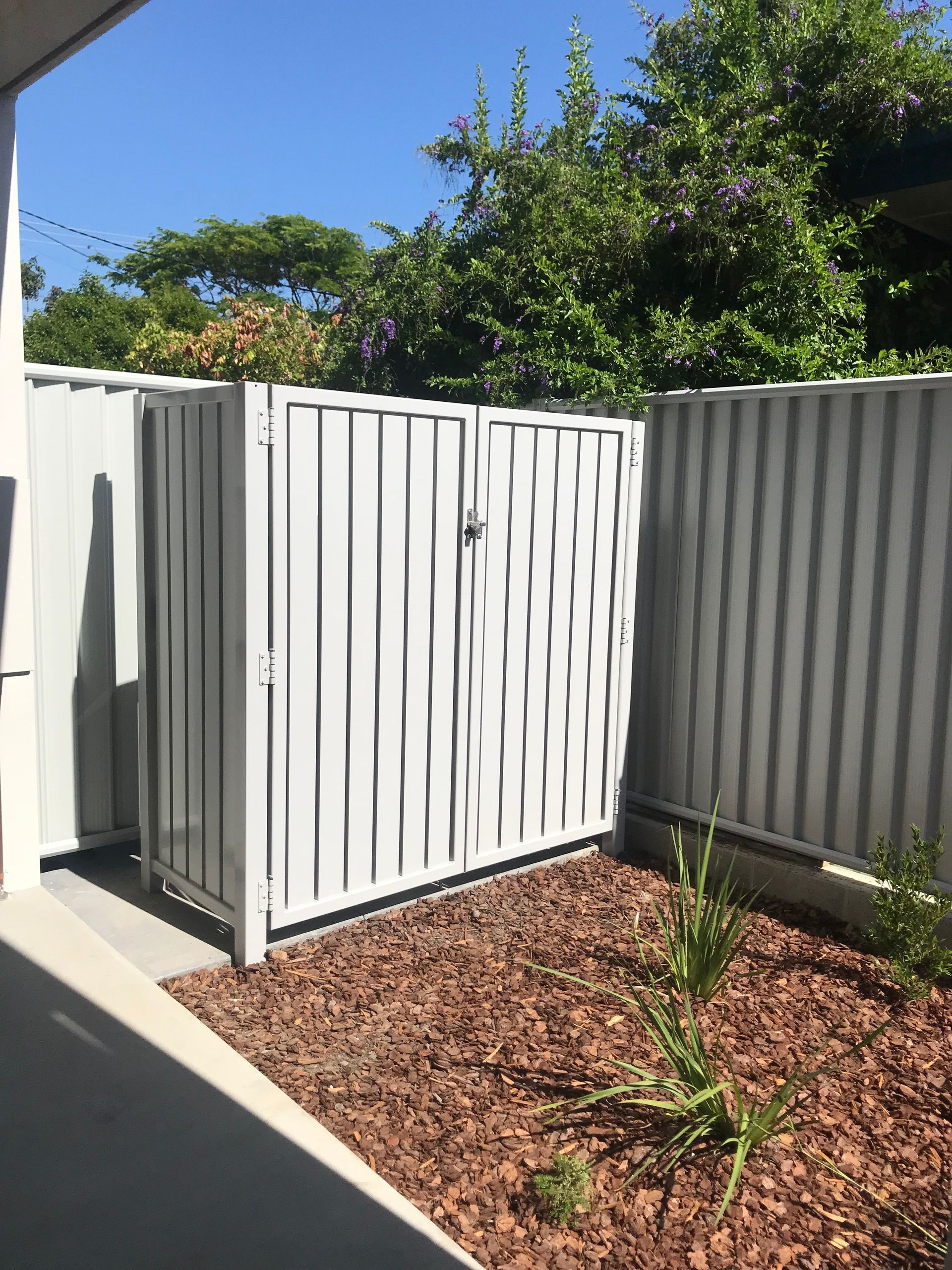 A white gate is sitting in the middle of a garden next to a fence — Fabricator In Coffs Harbour, NSW