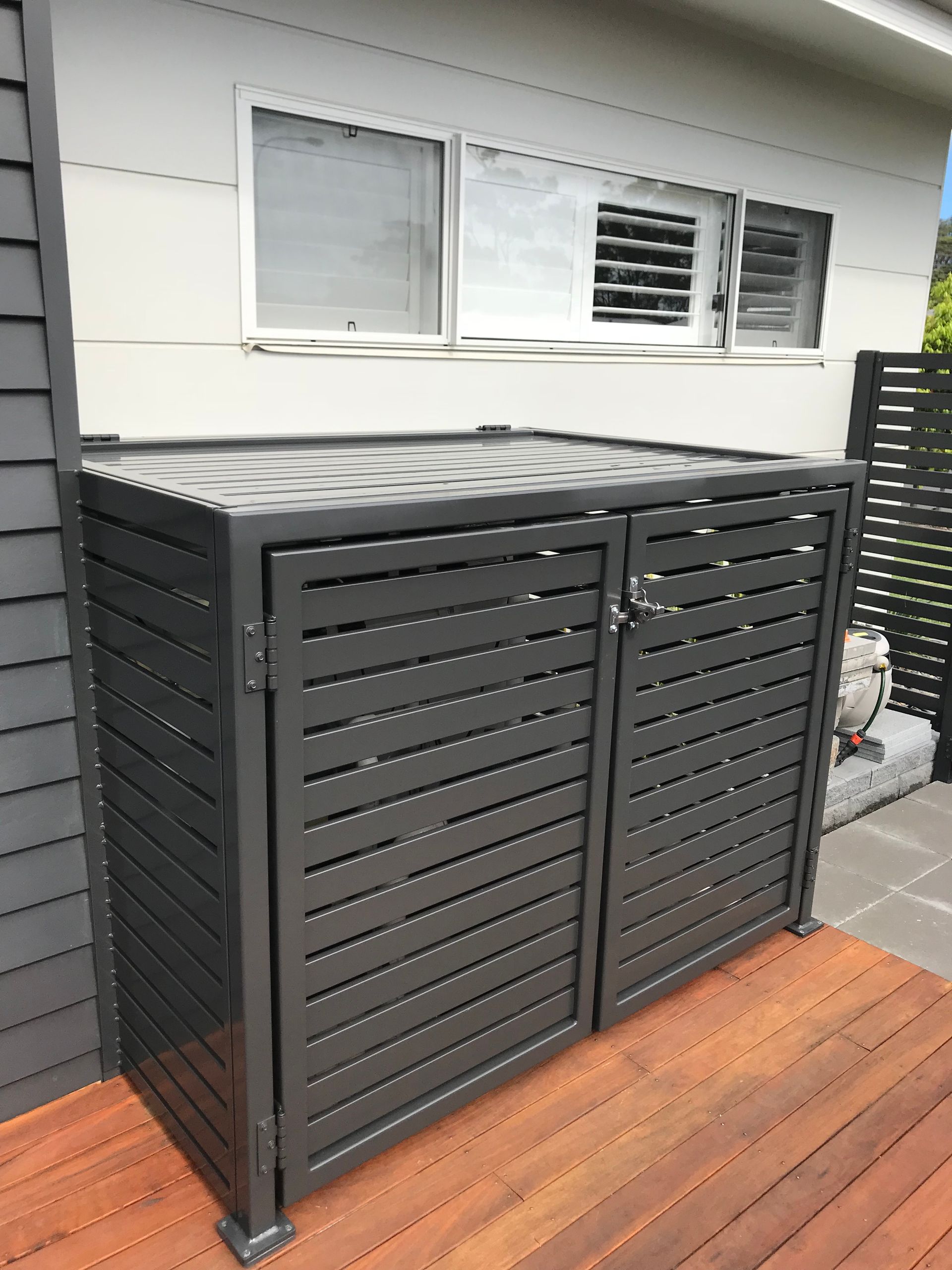 A black fence is sitting on a wooden deck in front of a house — Fabricator In Coffs Harbour, NSW