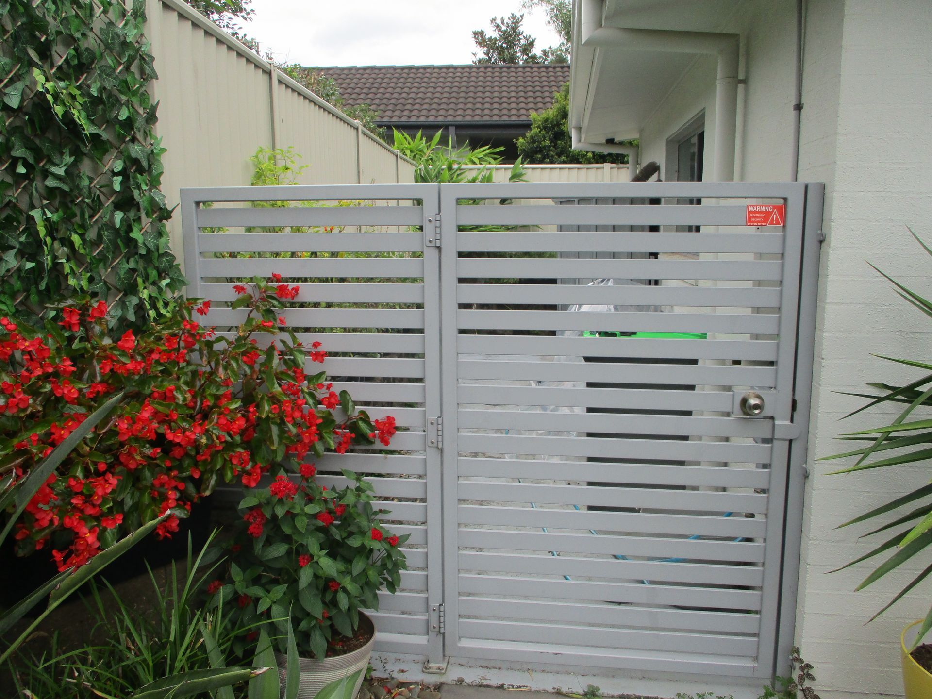 A white gate with red flowers in front of it — Fabricator In Coffs Harbour, NSW