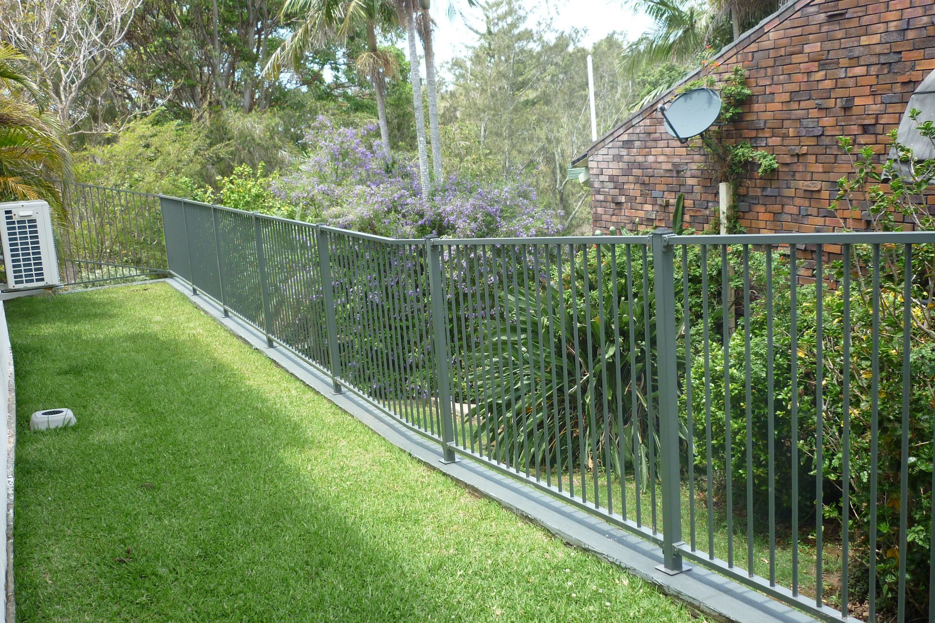 A metal fence surrounds a lush green lawn in front of a brick building — Fabricator In Coffs Harbour, NSW