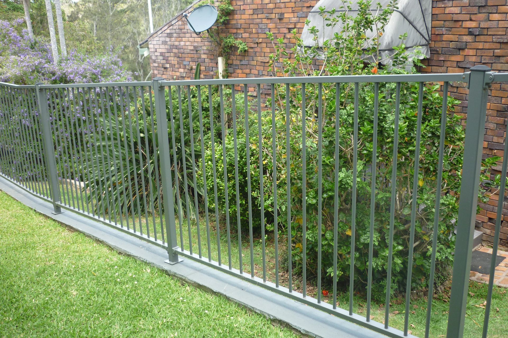A metal fence surrounds a lush green yard in front of a brick building — Fabricator In Coffs Harbour, NSW
