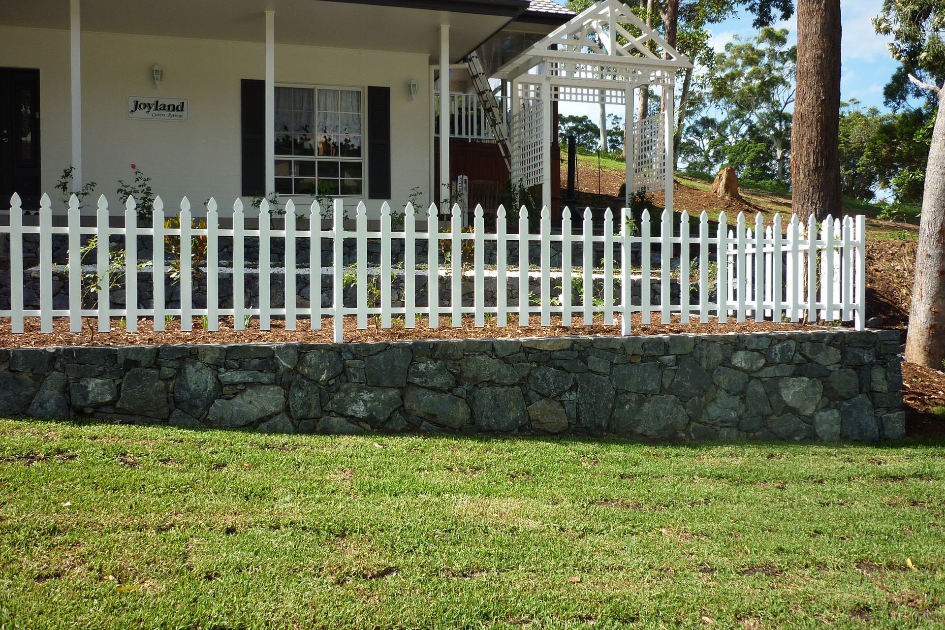 A white picket fence is in front of a house — Fabricator In Coffs Harbour, NSW