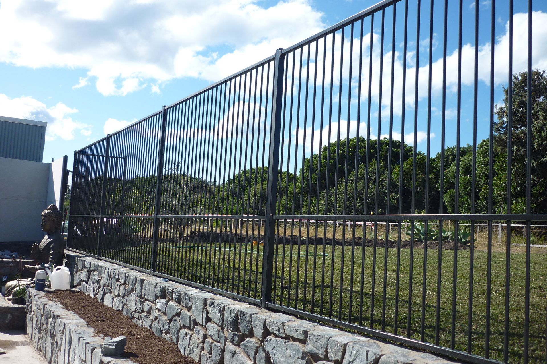 A black metal fence is surrounded by a stone wall — Fabricator In Coffs Harbour, NSW