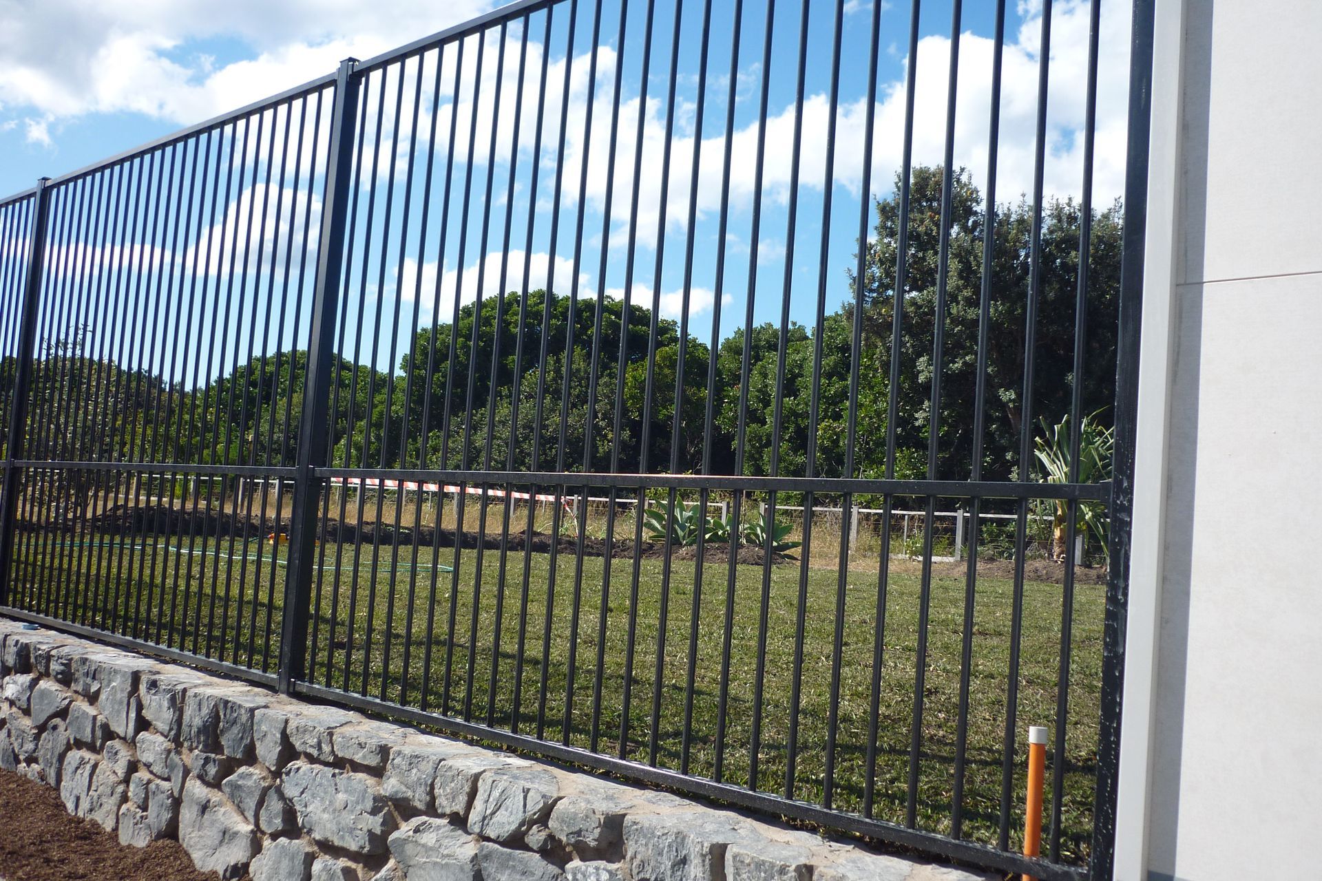 A black wrought iron fence surrounds a stone wall — Fabricator In Coffs Harbour, NSW
