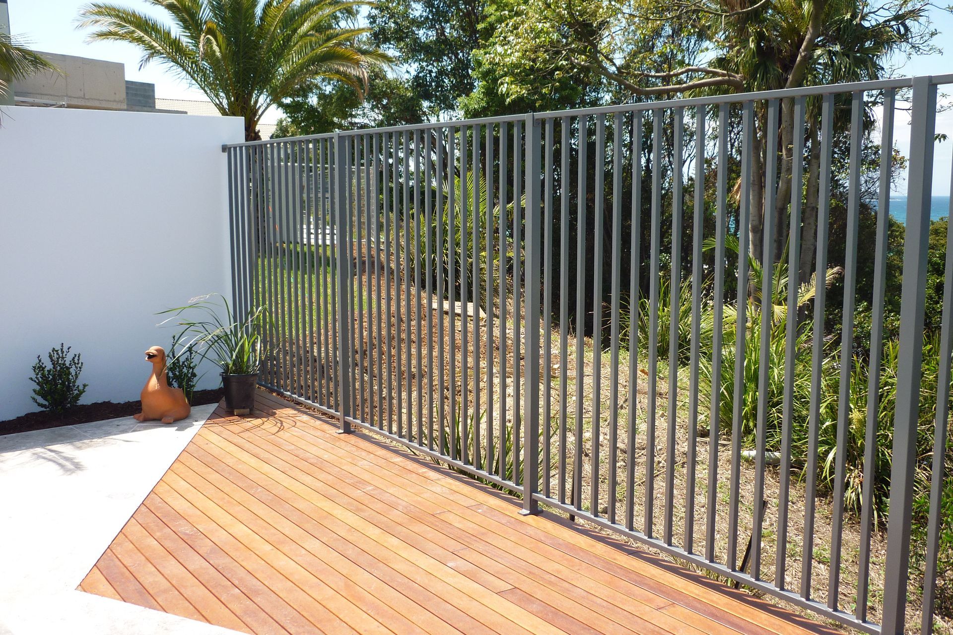 A metal fence surrounds a wooden deck with palm trees in the background — Fabricator In Coffs Harbour, NSW