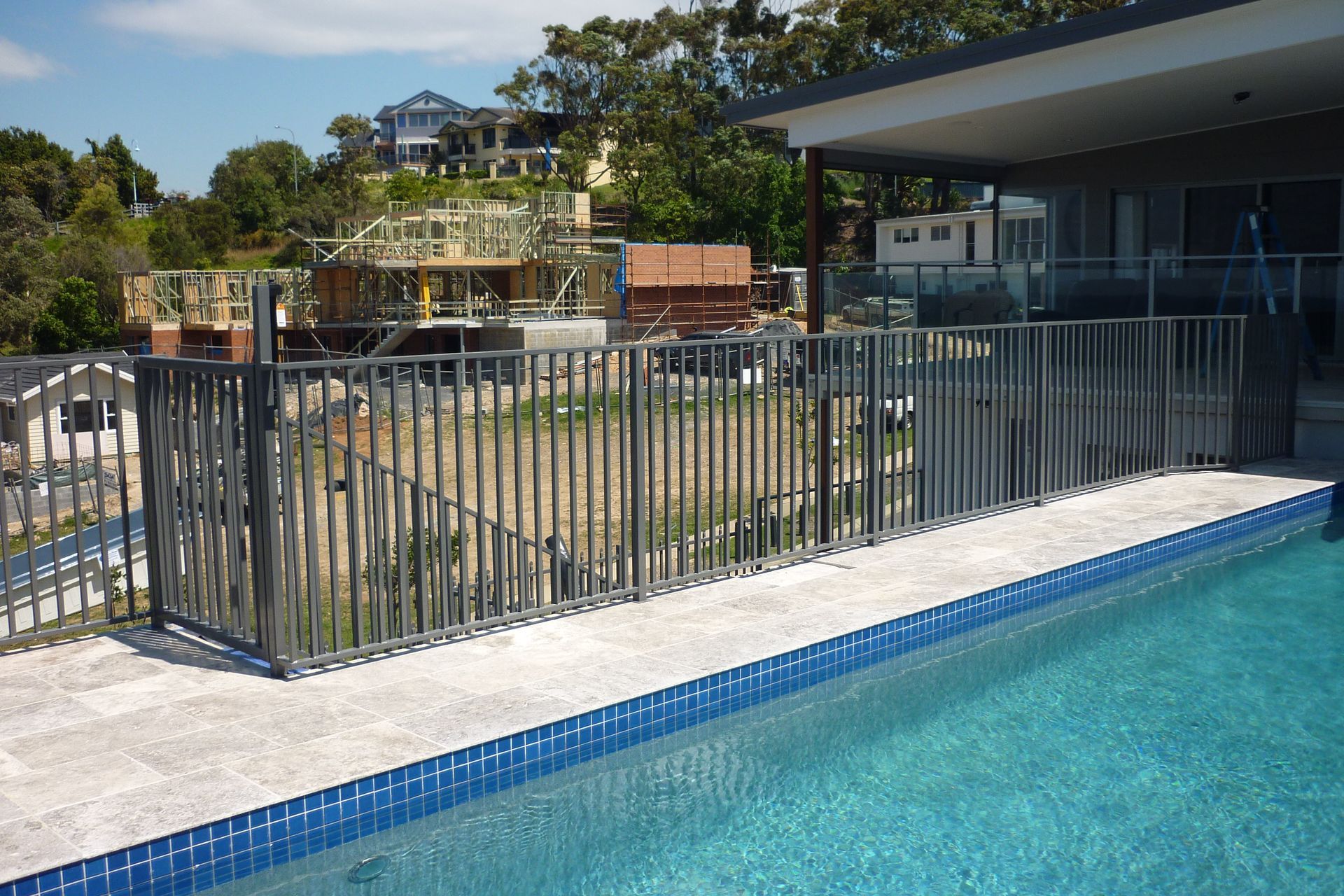 A fence surrounds a swimming pool with a house in the background — Fabricator In Coffs Harbour, NSW