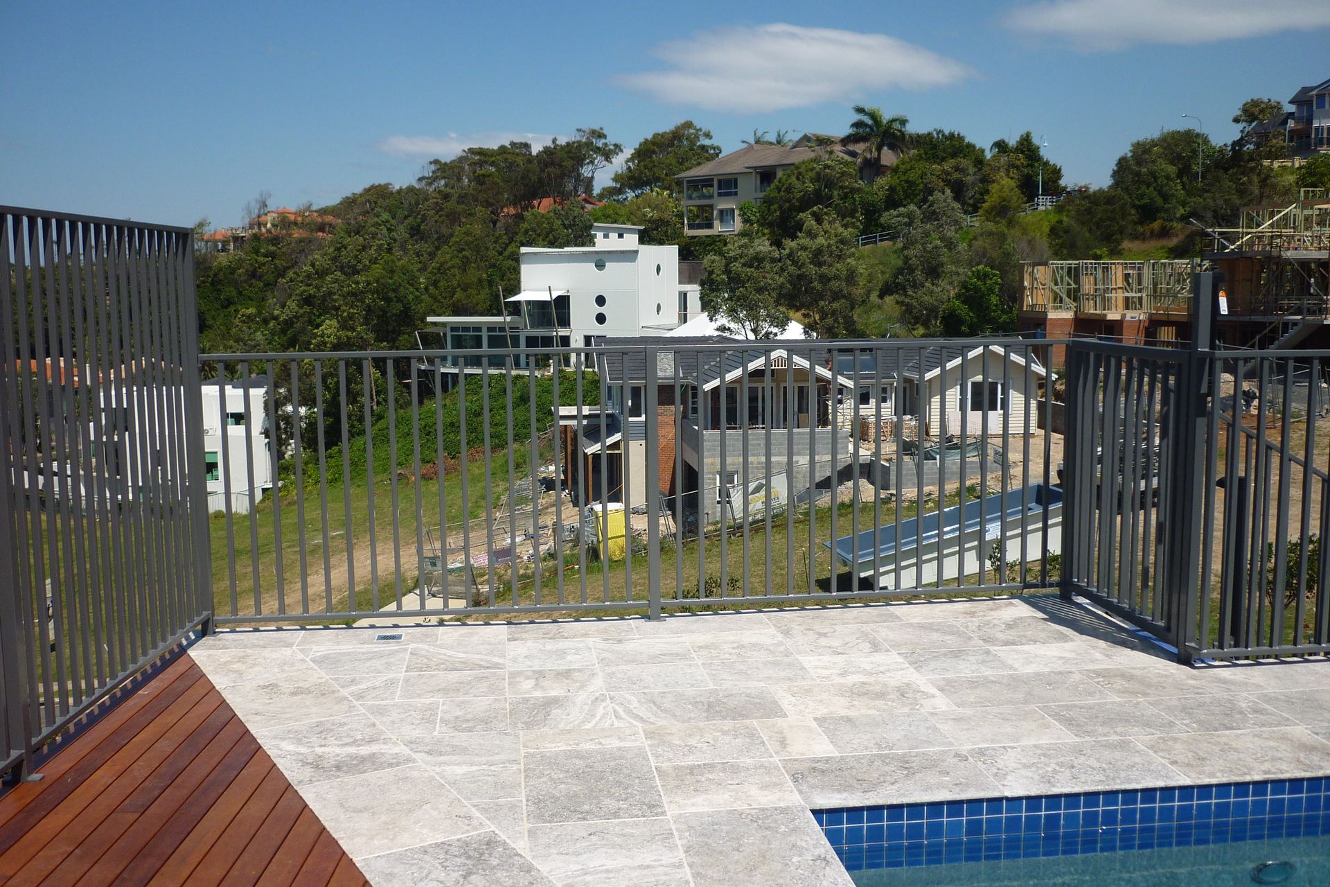 A fence surrounds a swimming pool with houses in the background — Fabricator In Coffs Harbour, NSW