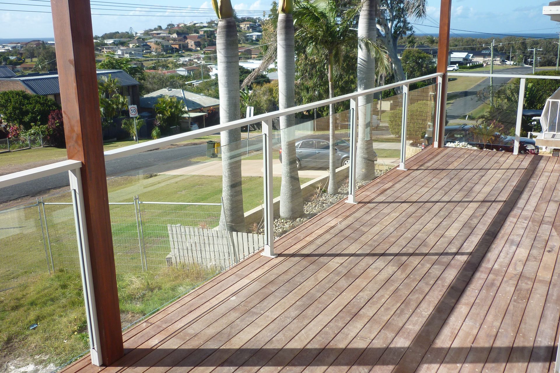 A wooden deck with a glass railing overlooking a city — Fabricator In Coffs Harbour, NSW
