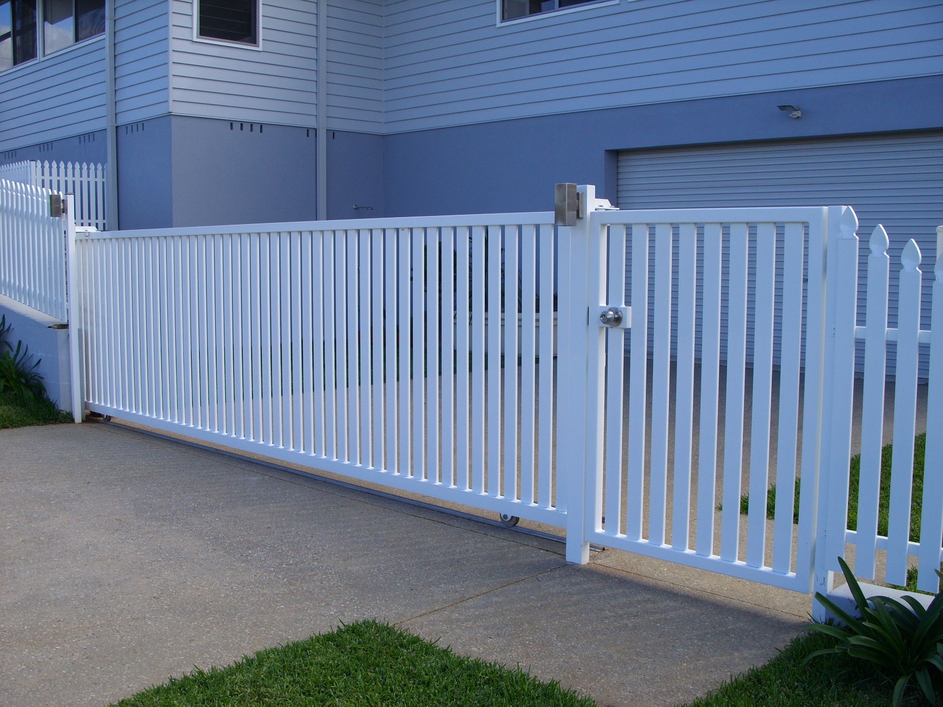 A white picket fence is in front of a blue house — Fabricator In Coffs Harbour, NSW