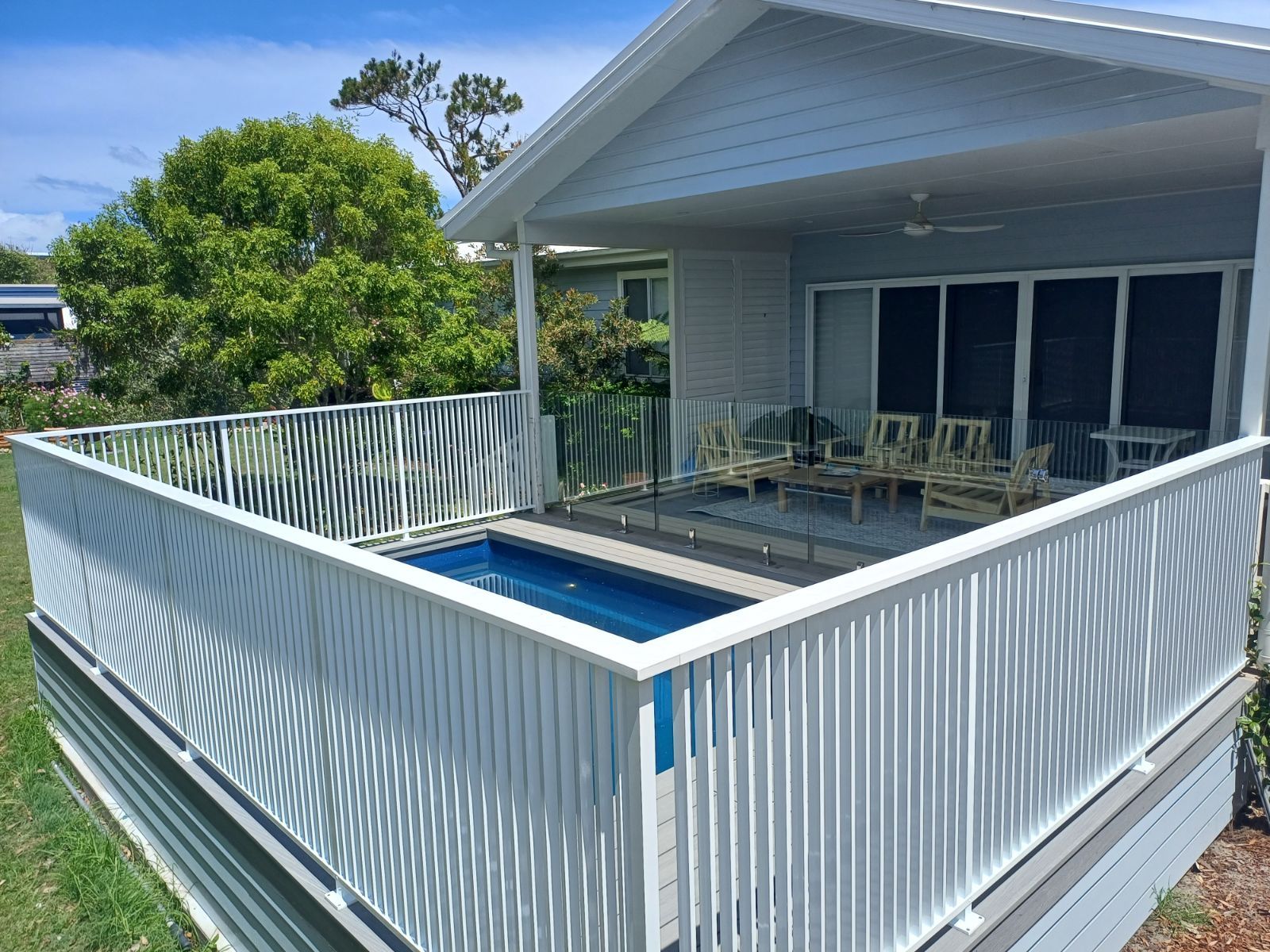 A white fence surrounds a swimming pool in front of a house — Fabricator In Coffs Harbour, NSW