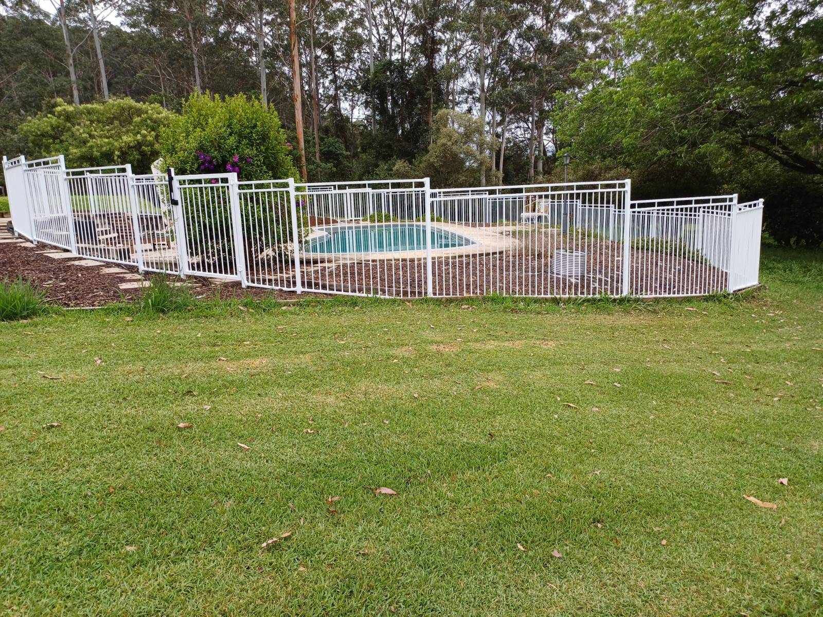 A white fence surrounds a swimming pool in a grassy field — Fabricator In Coffs Harbour, NSW