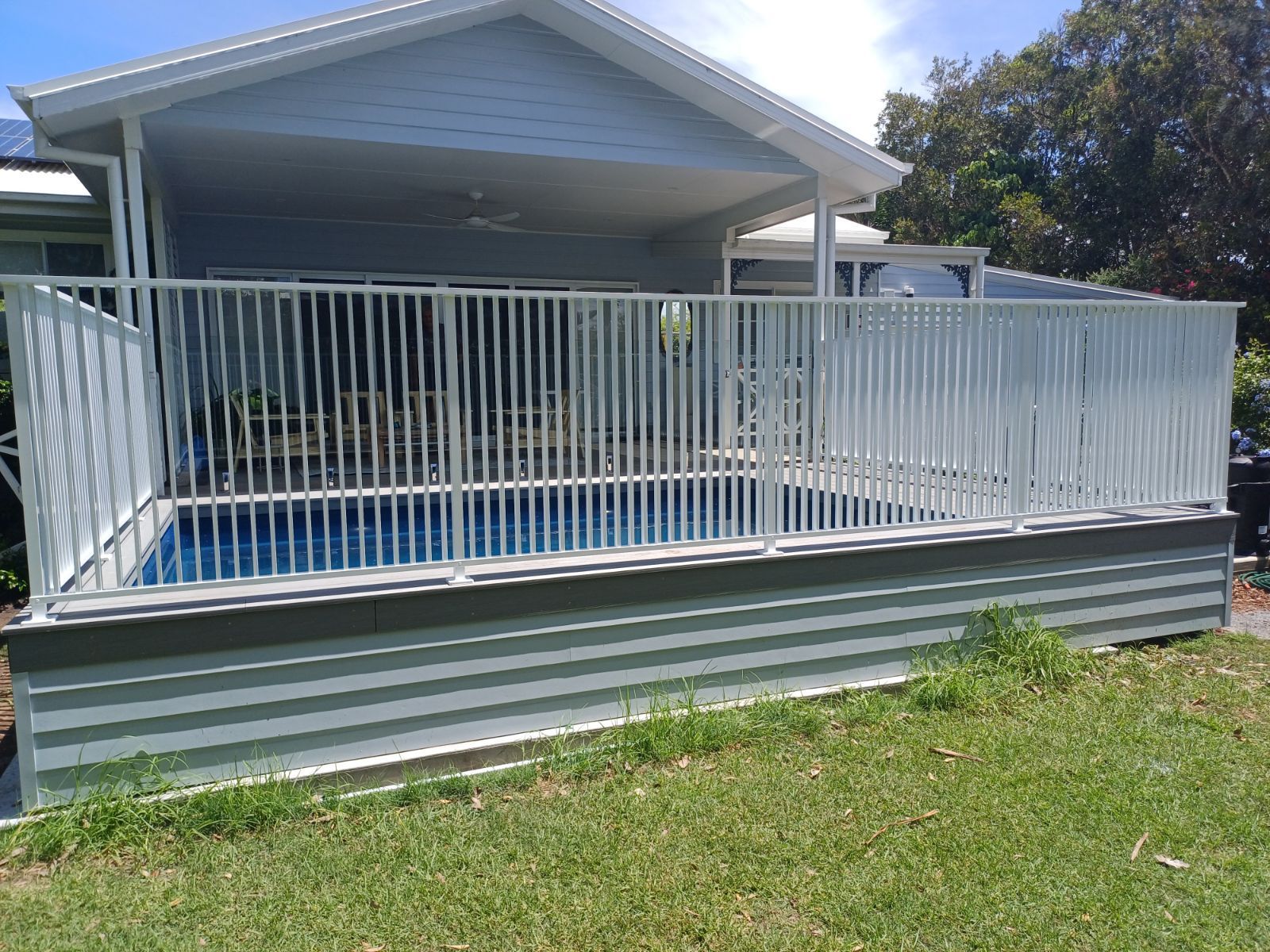 A white fence surrounds a swimming pool in front of a house — Fabricator In Coffs Harbour, NSW
