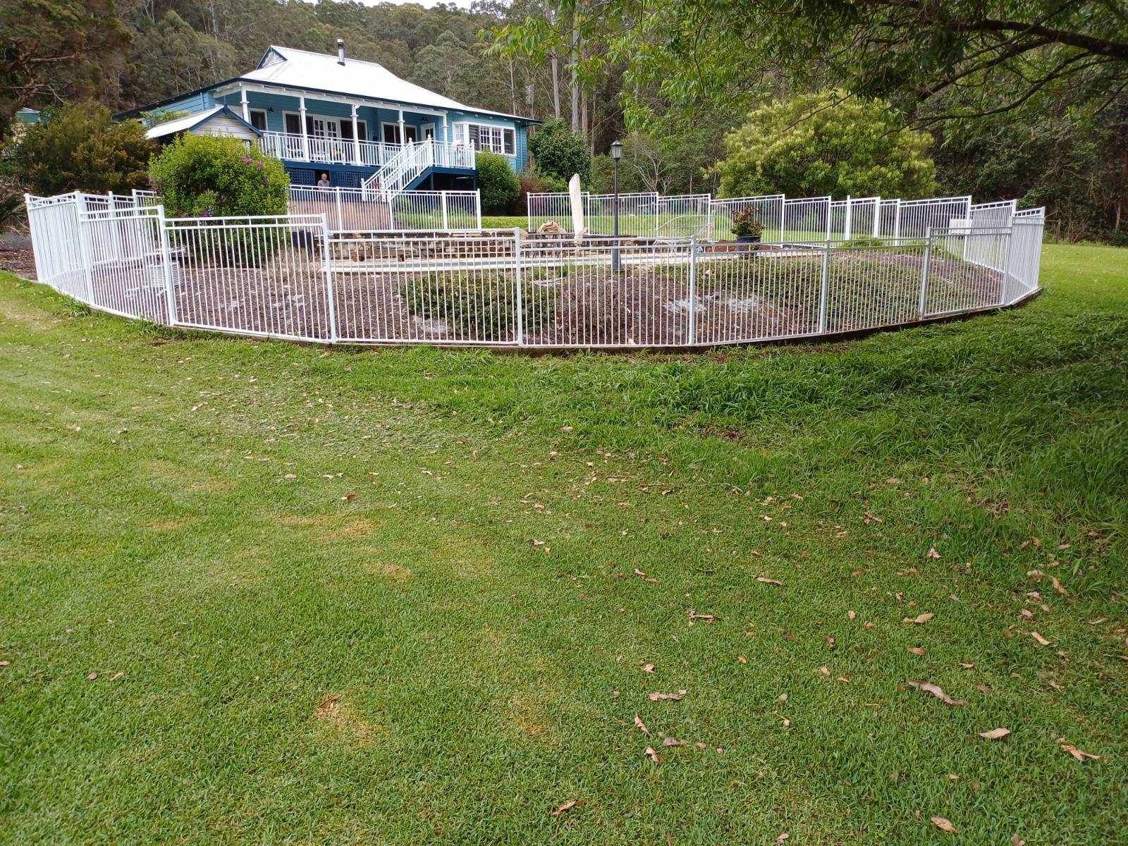 A white fence surrounds a large swimming pool in front of a house — Fabricator In Coffs Harbour, NSW
