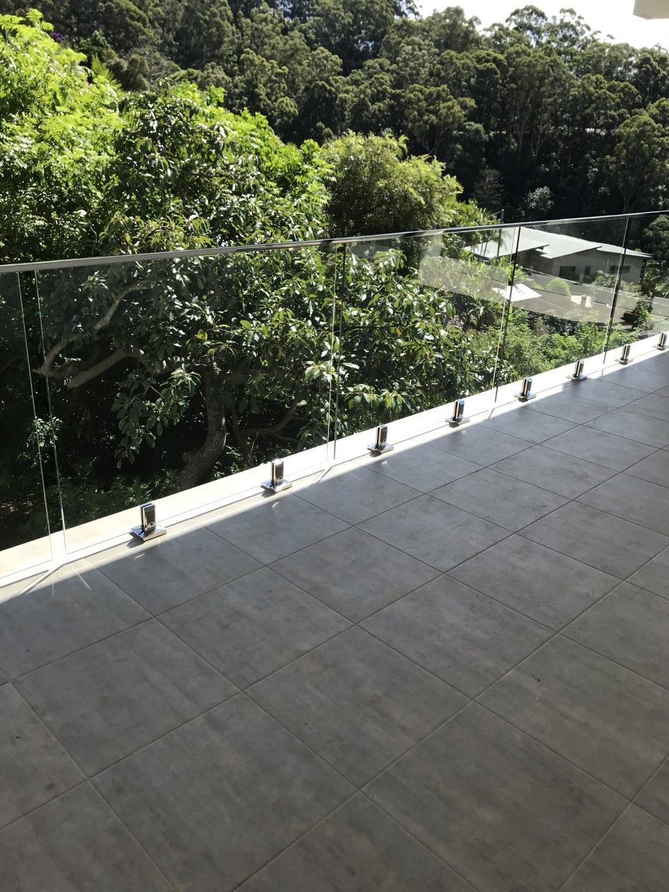 A balcony with a glass railing and trees in the background — Fabricator In Coffs Harbour, NSW