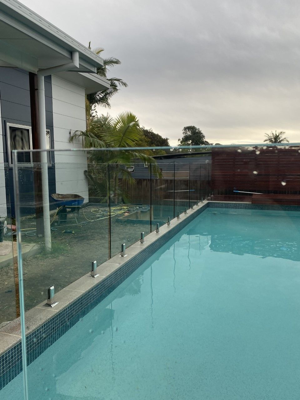 A swimming pool with a glass fence and a house in the background — Fabricator In Coffs Harbour, NSW