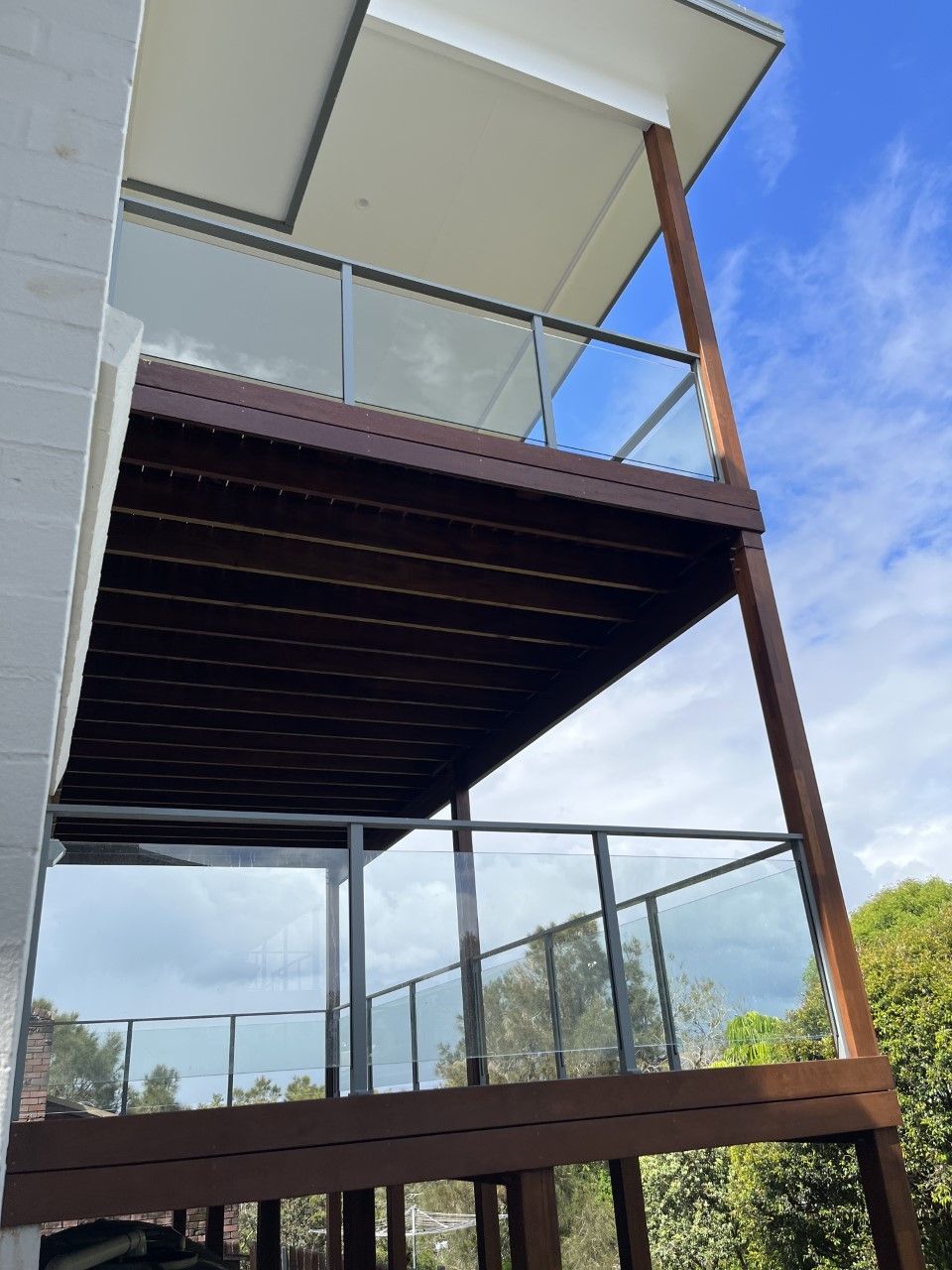 A balcony with a glass railing and a wooden deck — Fabricator In Coffs Harbour, NSW