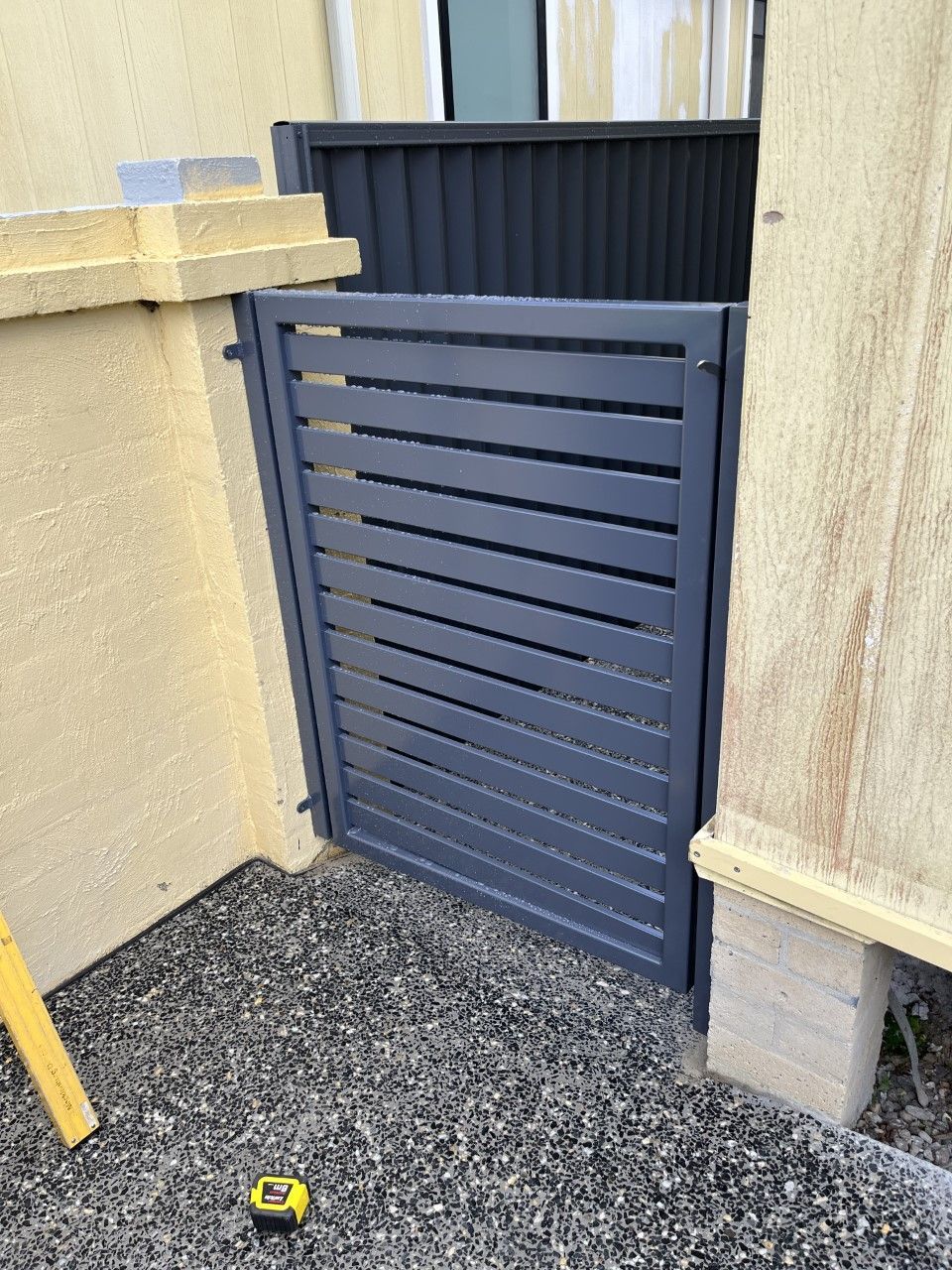 A black gate is sitting in front of a building next to a tape measure — Fabricator In Coffs Harbour, NSW
