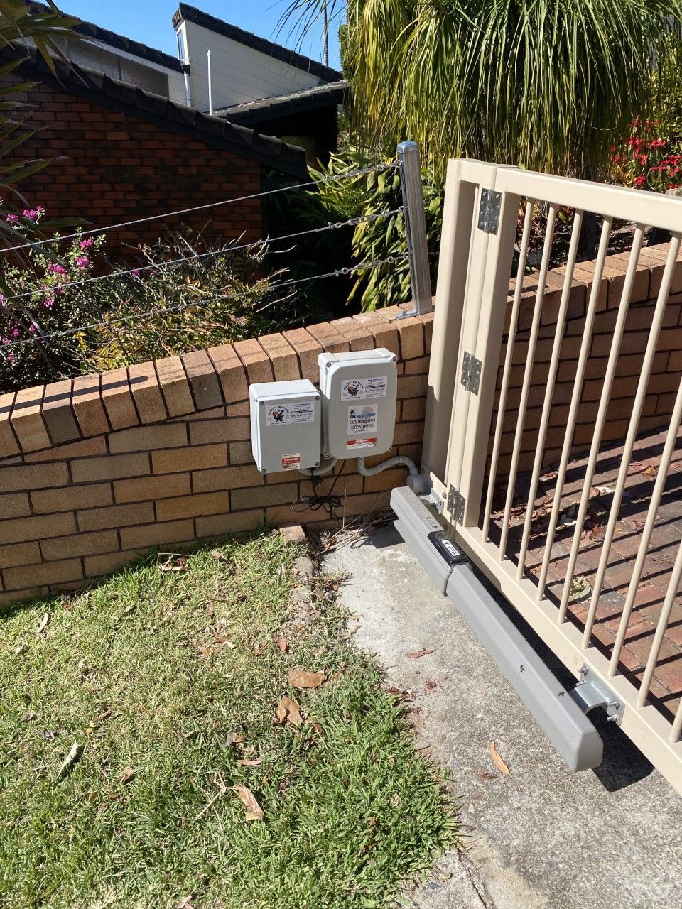 A sliding gate with a motor attached to it is sitting next to a brick wall — Fabricator In Coffs Harbour, NSW