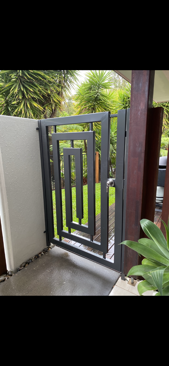 A black metal gate is sitting next to a white wall — Fabricator In Coffs Harbour, NSW