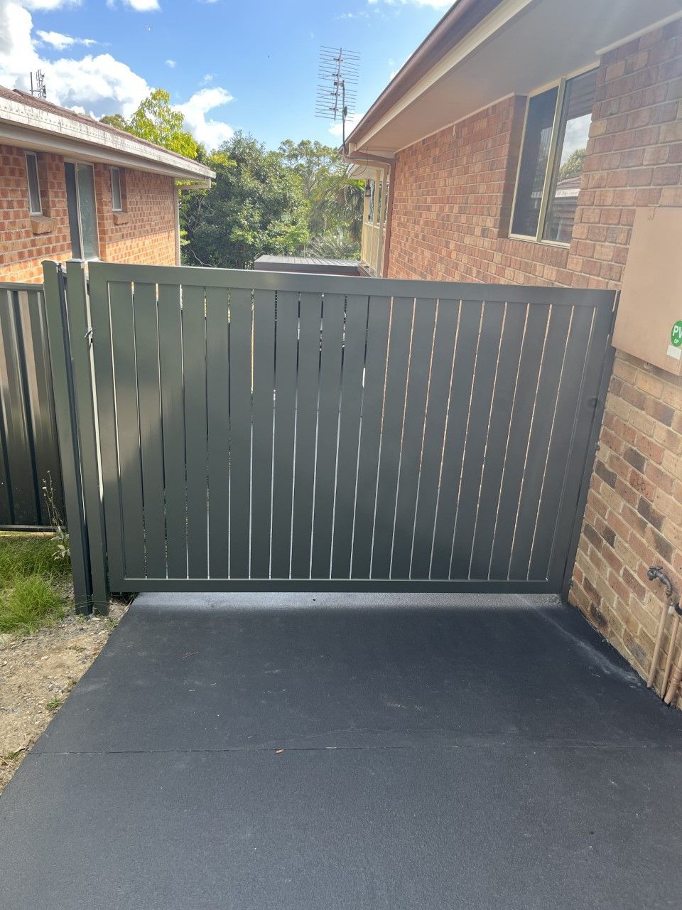 A black fence is sitting in front of a brick house — Fabricator In Coffs Harbour, NSW