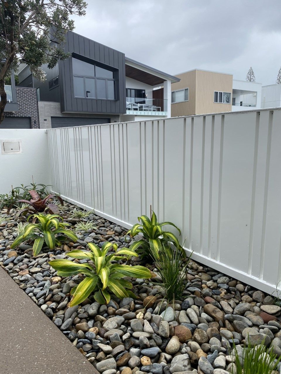 A white fence is surrounded by rocks and plants in front of a house — Fabricator In Coffs Harbour, NSW