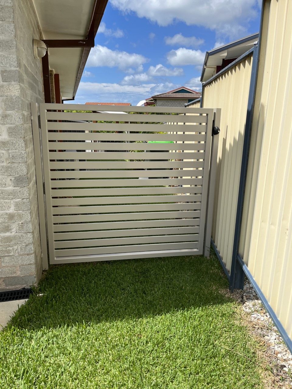 A white gate is sitting in the grass next to a fence — Fabricator In Coffs Harbour, NSW
