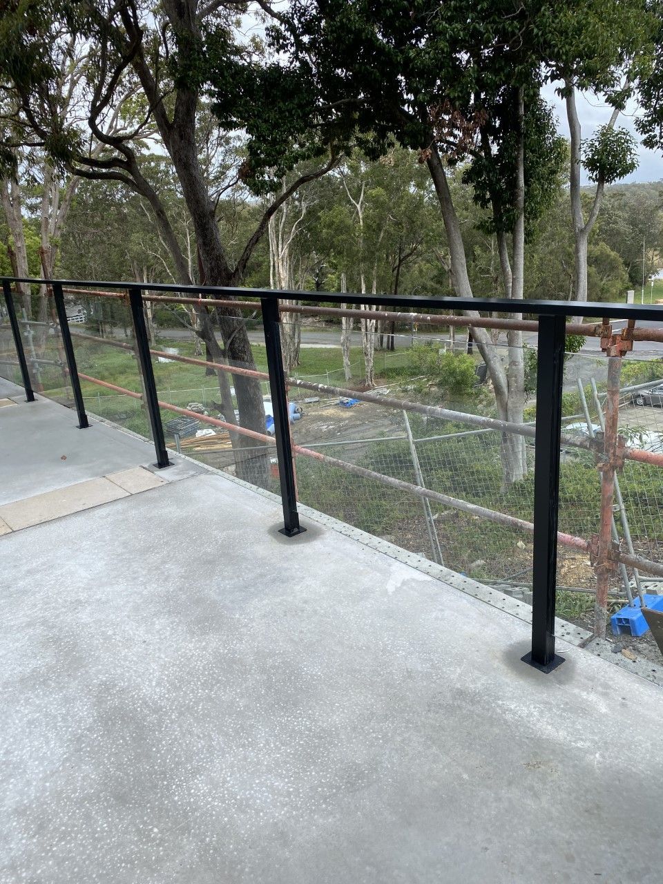 A balcony with a glass railing and trees in the background — Fabricator In Coffs Harbour, NSW