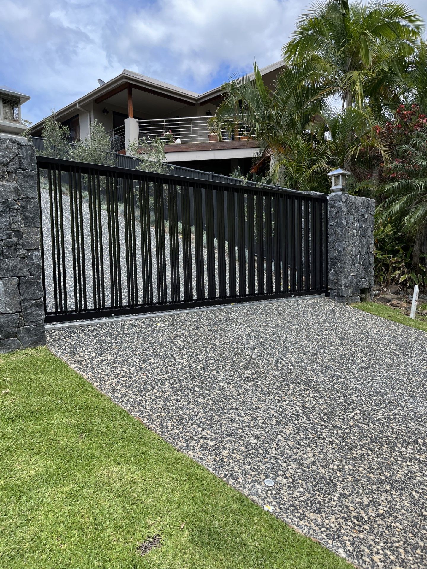 A black sliding gate is leading to a large house — Fabricator In Coffs Harbour, NSW