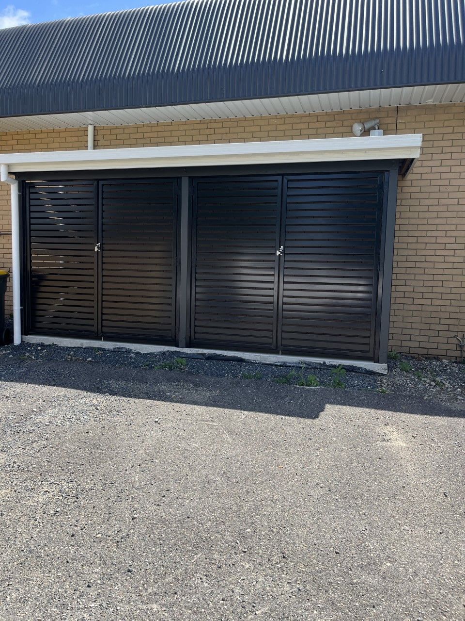 A black garage door is sitting in front of a brick building — Fabricator In Coffs Harbour, NSW